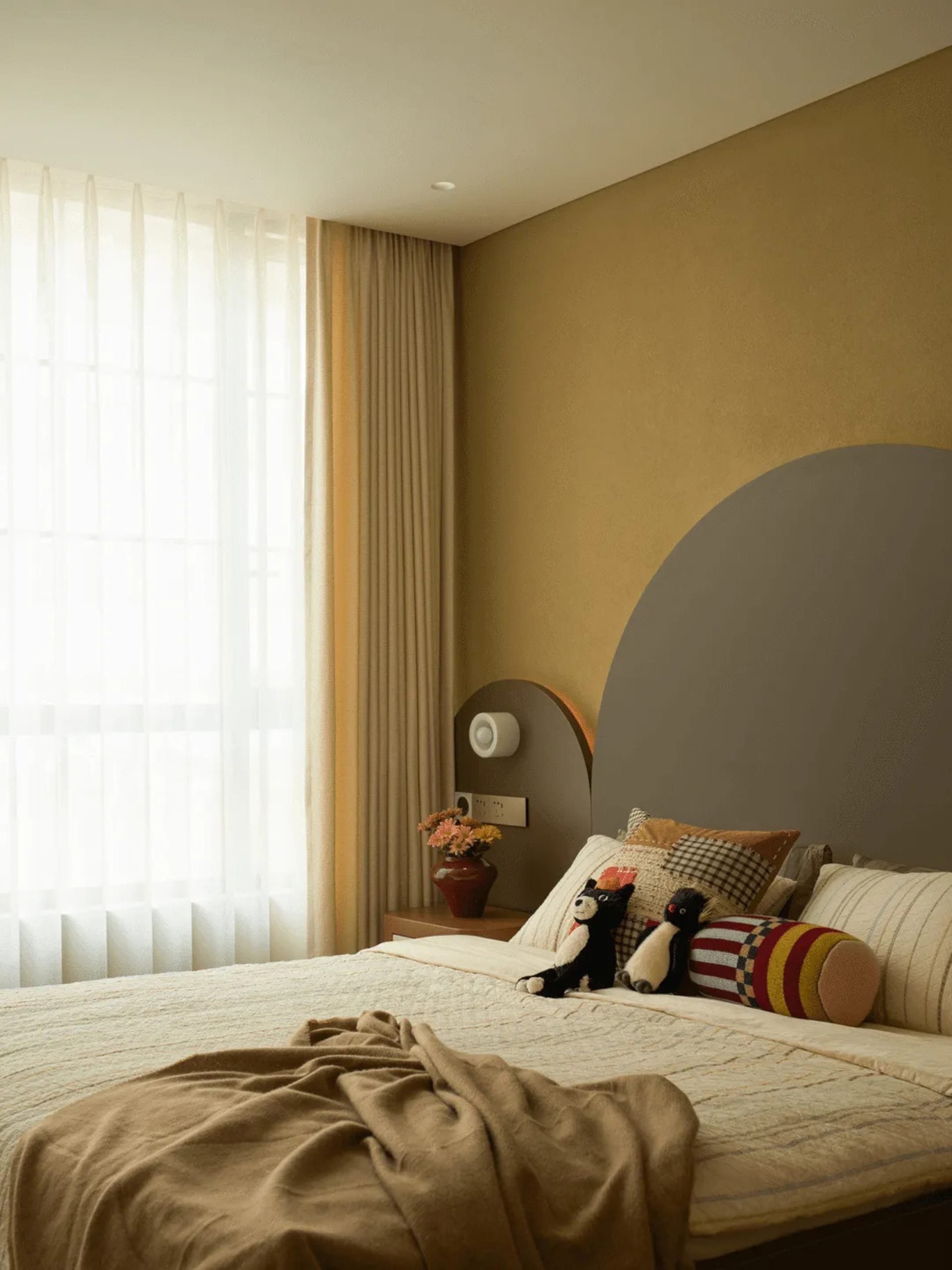 Cozy bedroom with a bed, mirror, and window, featuring a yellow wall, a blanket, pillows, and stuffed animals