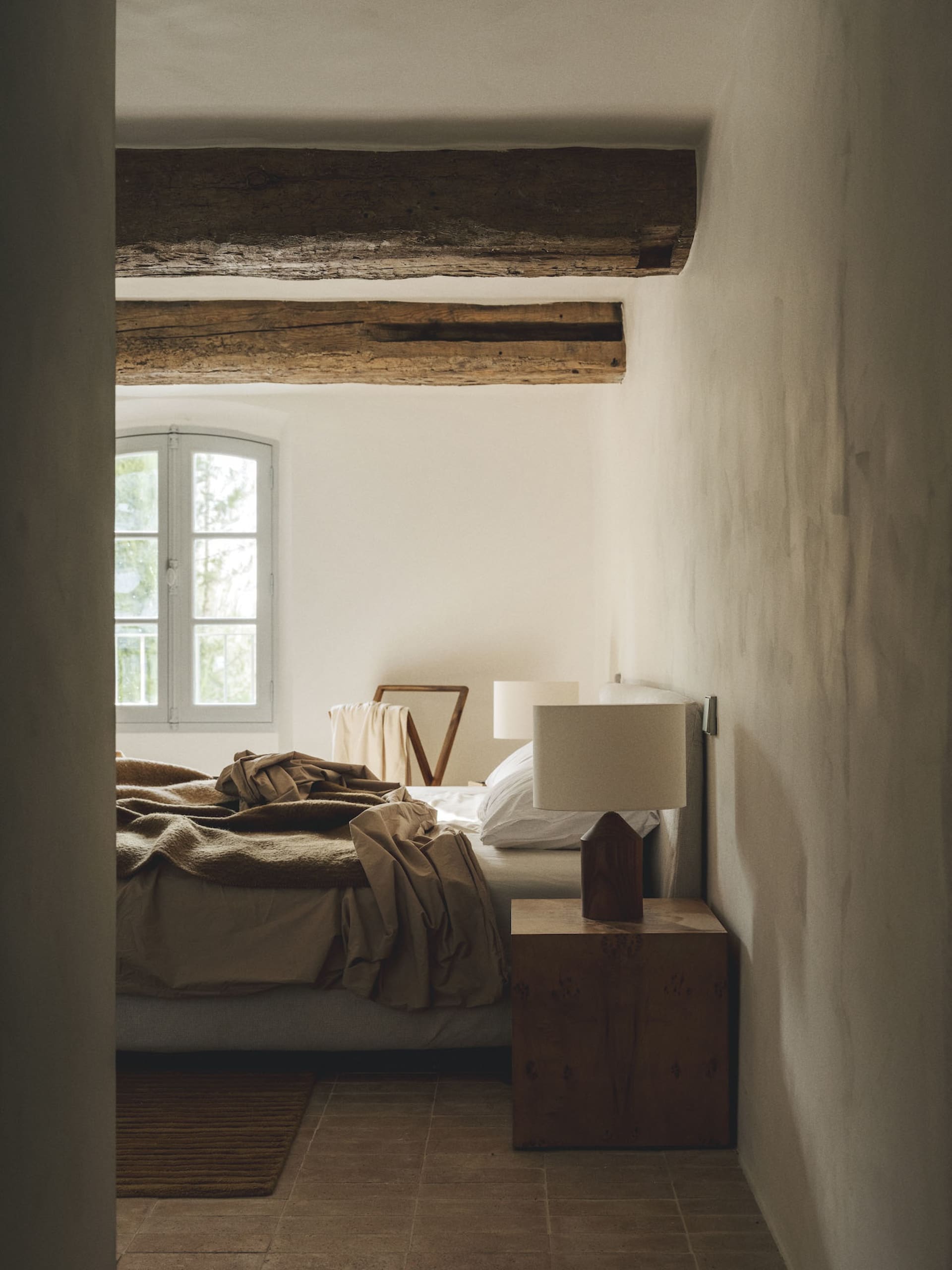 Cozy bedroom with a bed, chair, and lamp, surrounded by stone walls and dimly lit