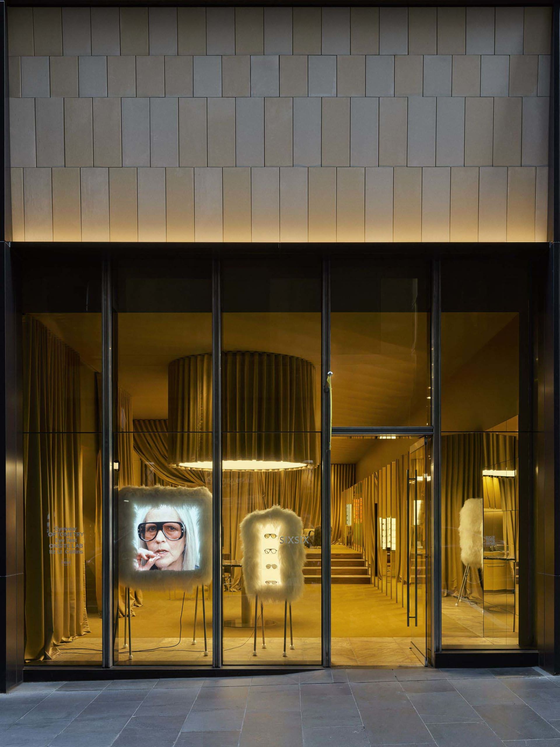 A clothing store display window featuring a mannequin in sunglasses in front of a TV screen, set in a well-lit storefront