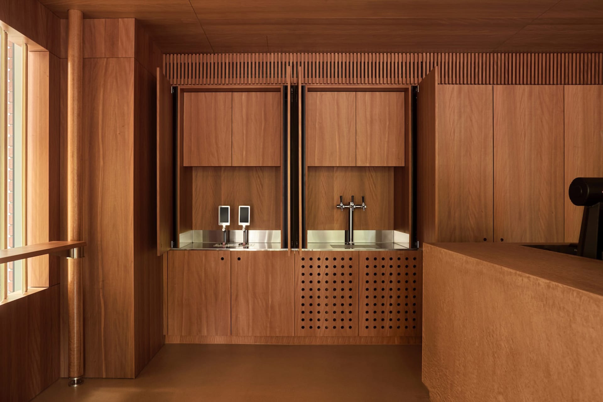 A well-organized kitchen with wooden cabinets, a metal sink, and a brown color scheme, lit by natural light