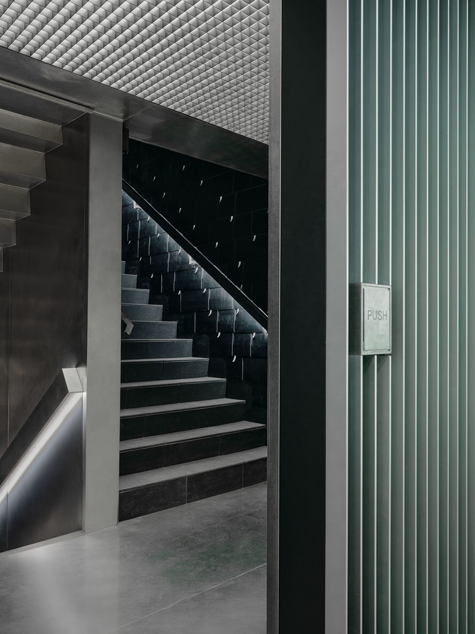A dimly lit stairwell with concrete steps and a black and white color scheme, featuring a glass door in the background