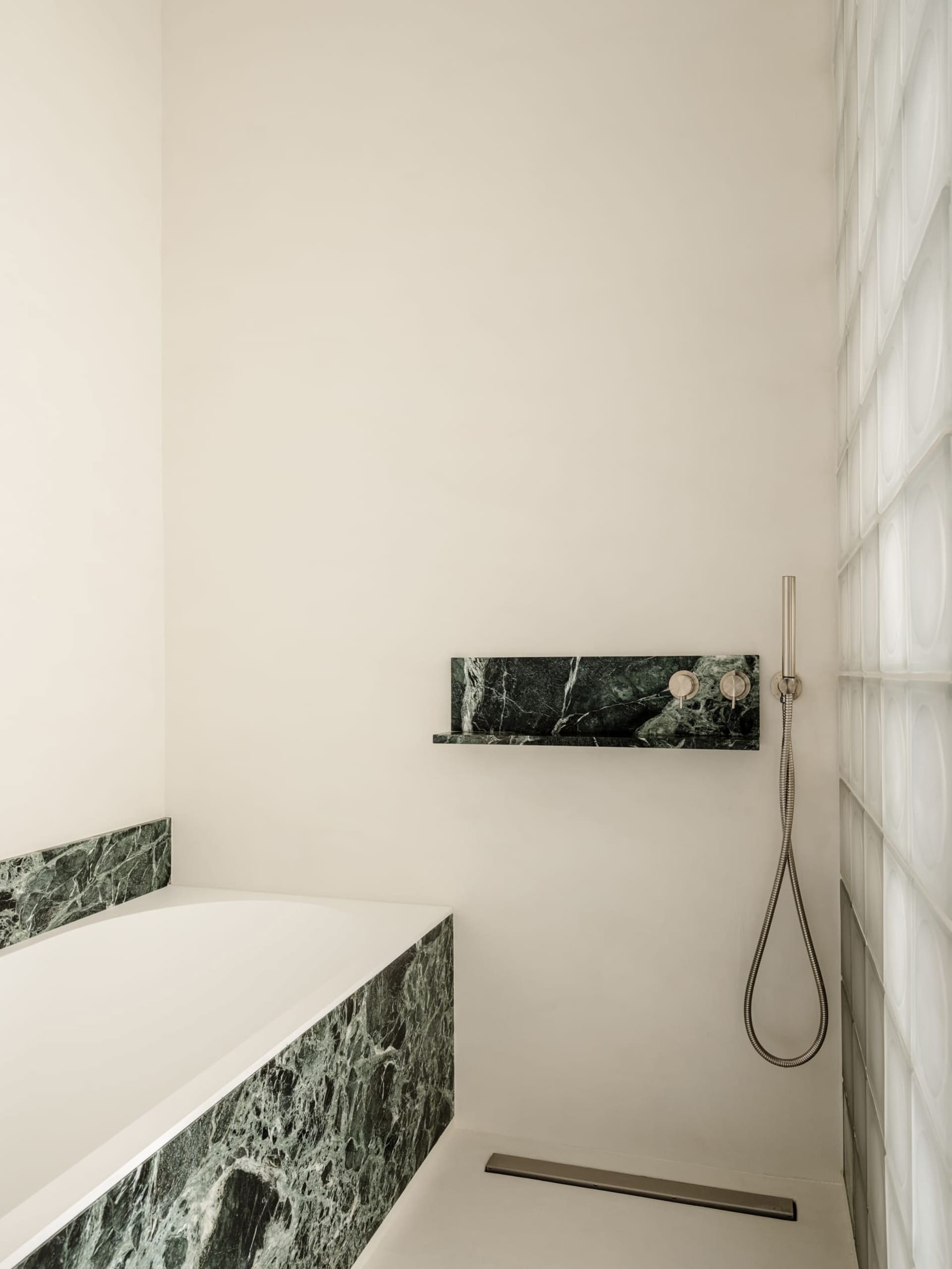 Modern bathroom with a white bathtub, shower, and marble countertop, set in a dimly lit space with clean lines and minimalistic design elements
