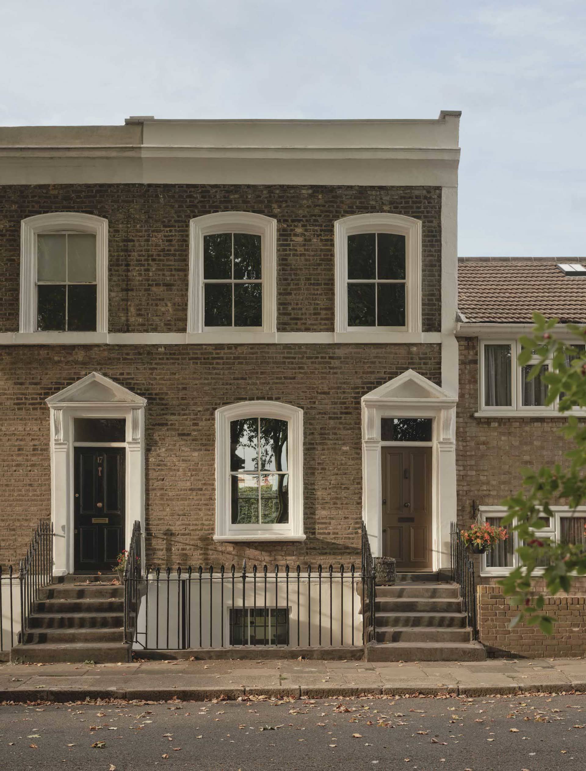A historic brick building with a white trim and a balcony on the second floor, set in a city with a street in the background
