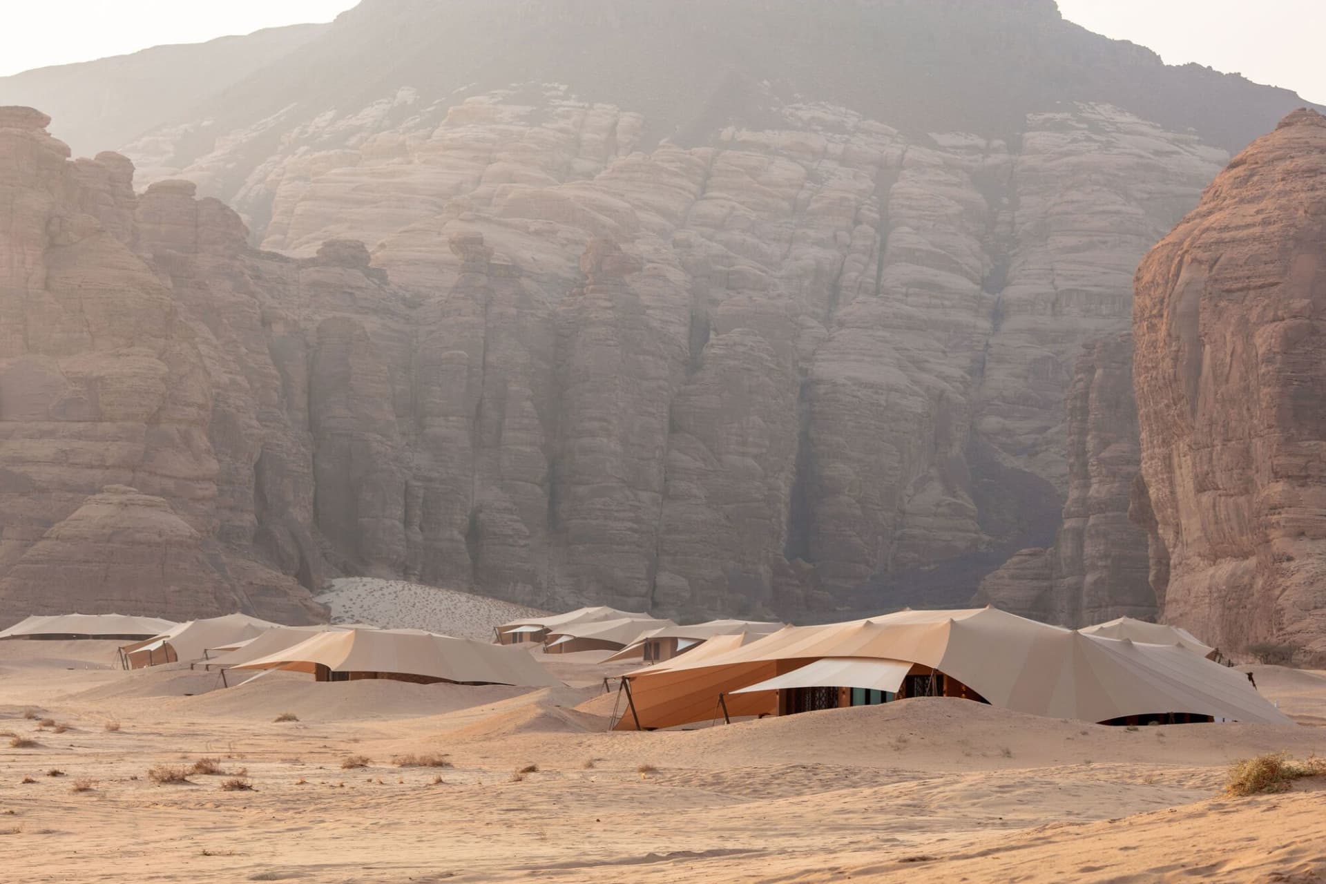 A desert landscape with a mountain in the background, featuring several tents of varying sizes and angles, creating a sense of depth and complexity