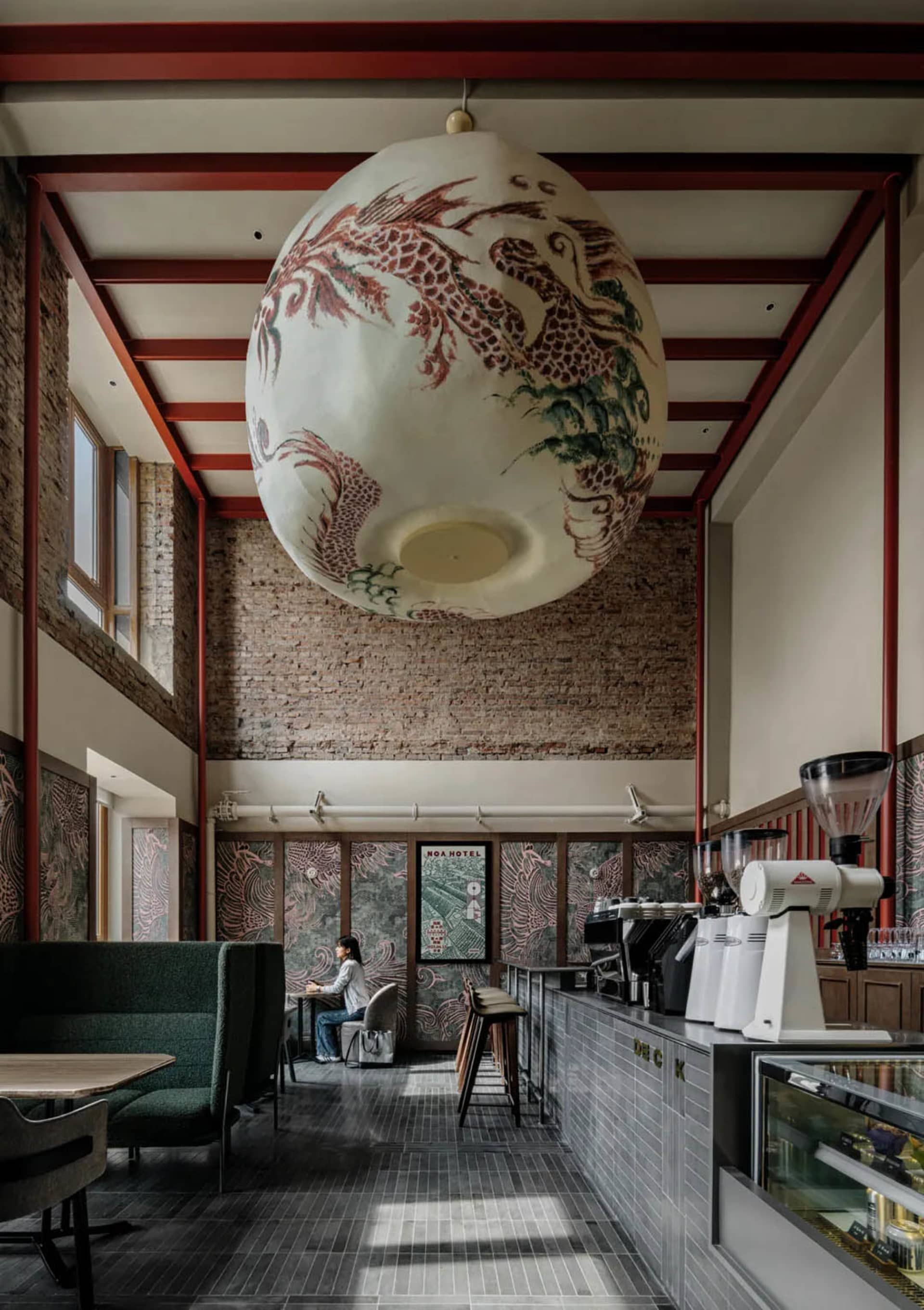 A warm and inviting restaurant interior with brick walls, wooden furniture, and soft lighting, featuring a large open space with a high ceiling and artwork on the walls