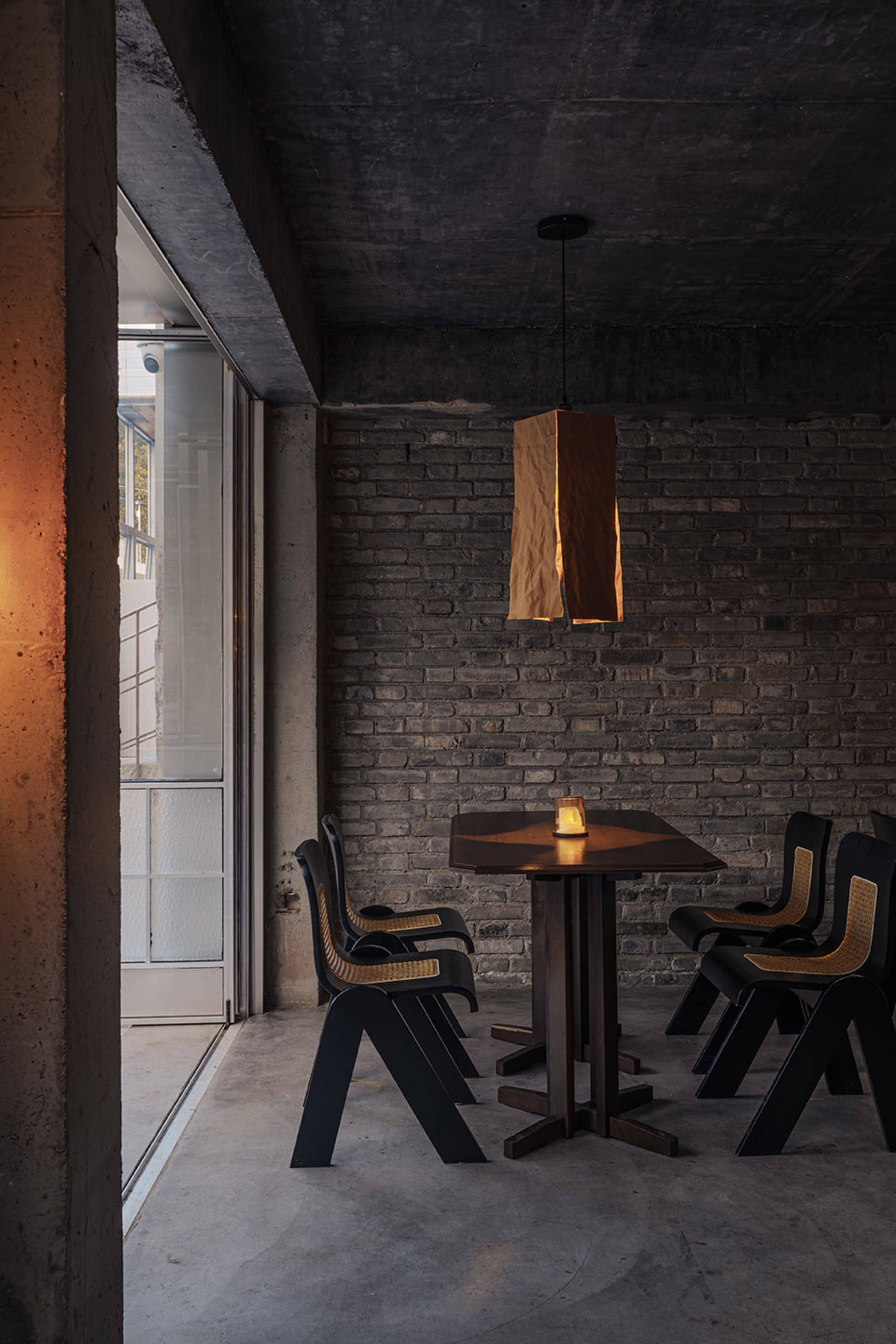 Cozy dining area with a brown table, black chairs, and a brick wall, dimly lit for an intimate atmosphere