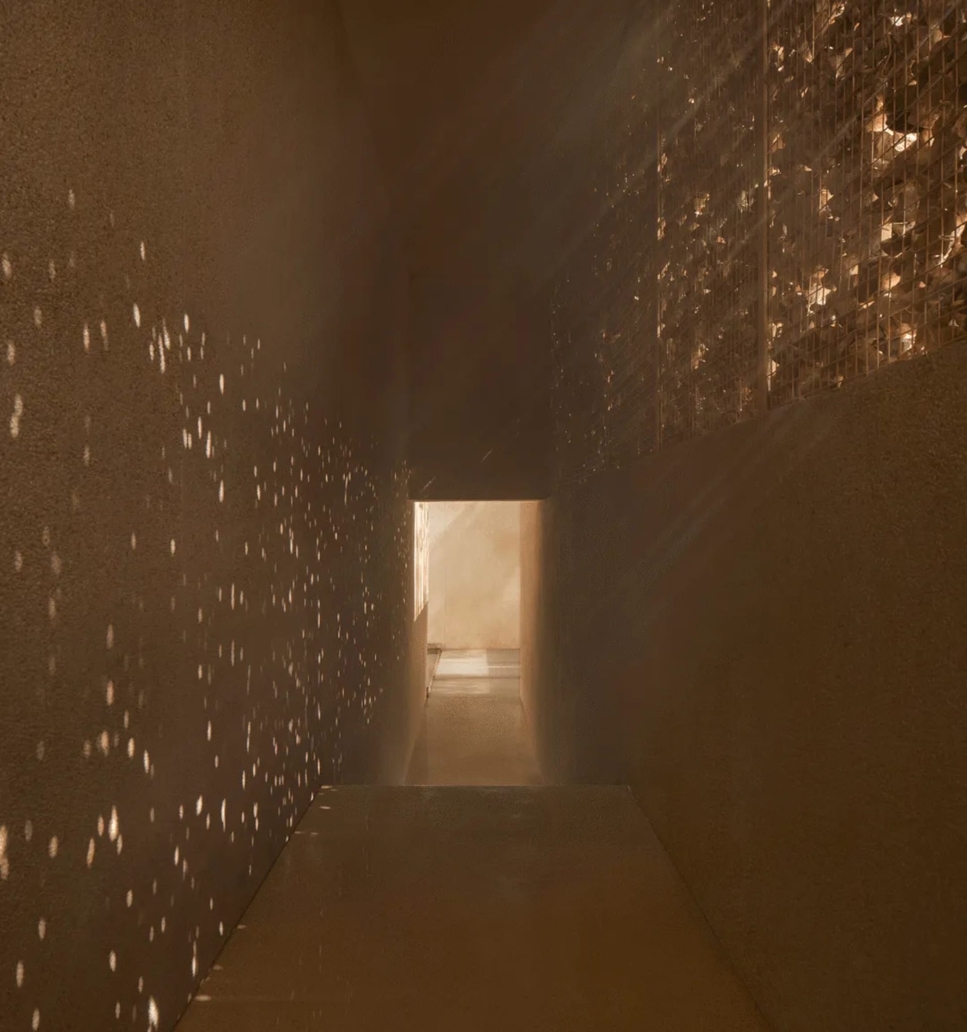 A simple functional hallway with concrete walls, lights on the wall, and a doorway leading to another room, creating a warm and inviting atmosphere
