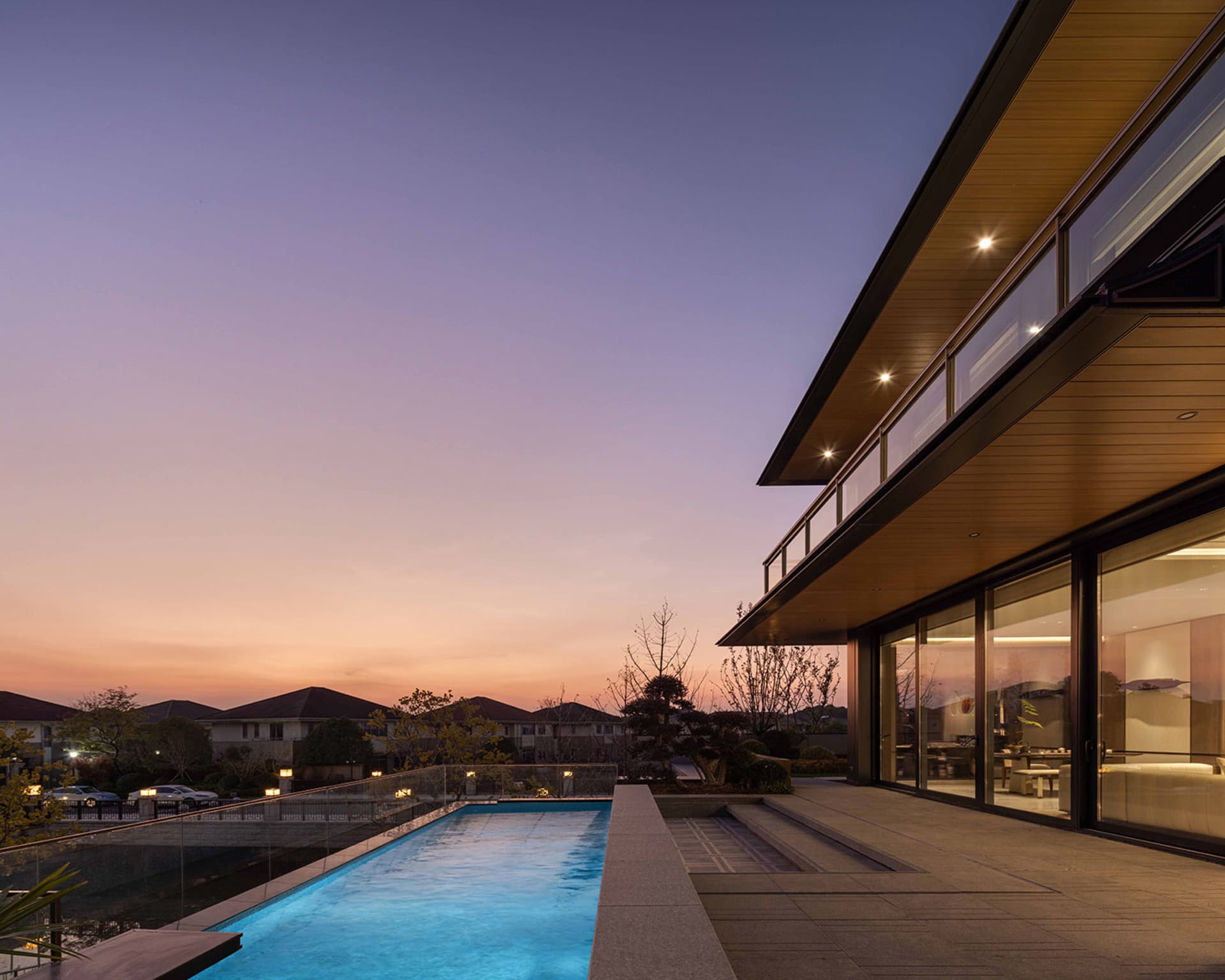 A modern house with a wooden facade, a blue pool, and a deck, set against a warm sunset backdrop