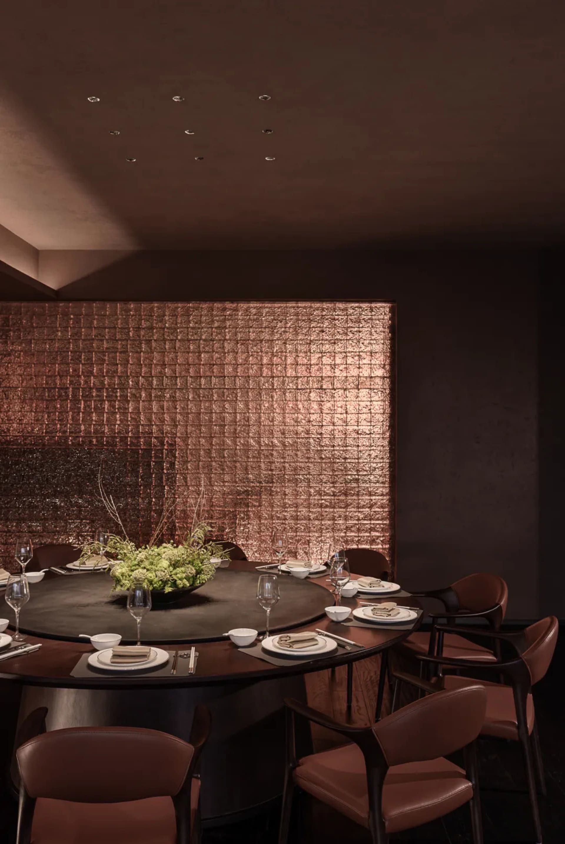 Cozy modern dining space with a round table, chairs, and a potted plant, set with plates, wine glasses, and utensils