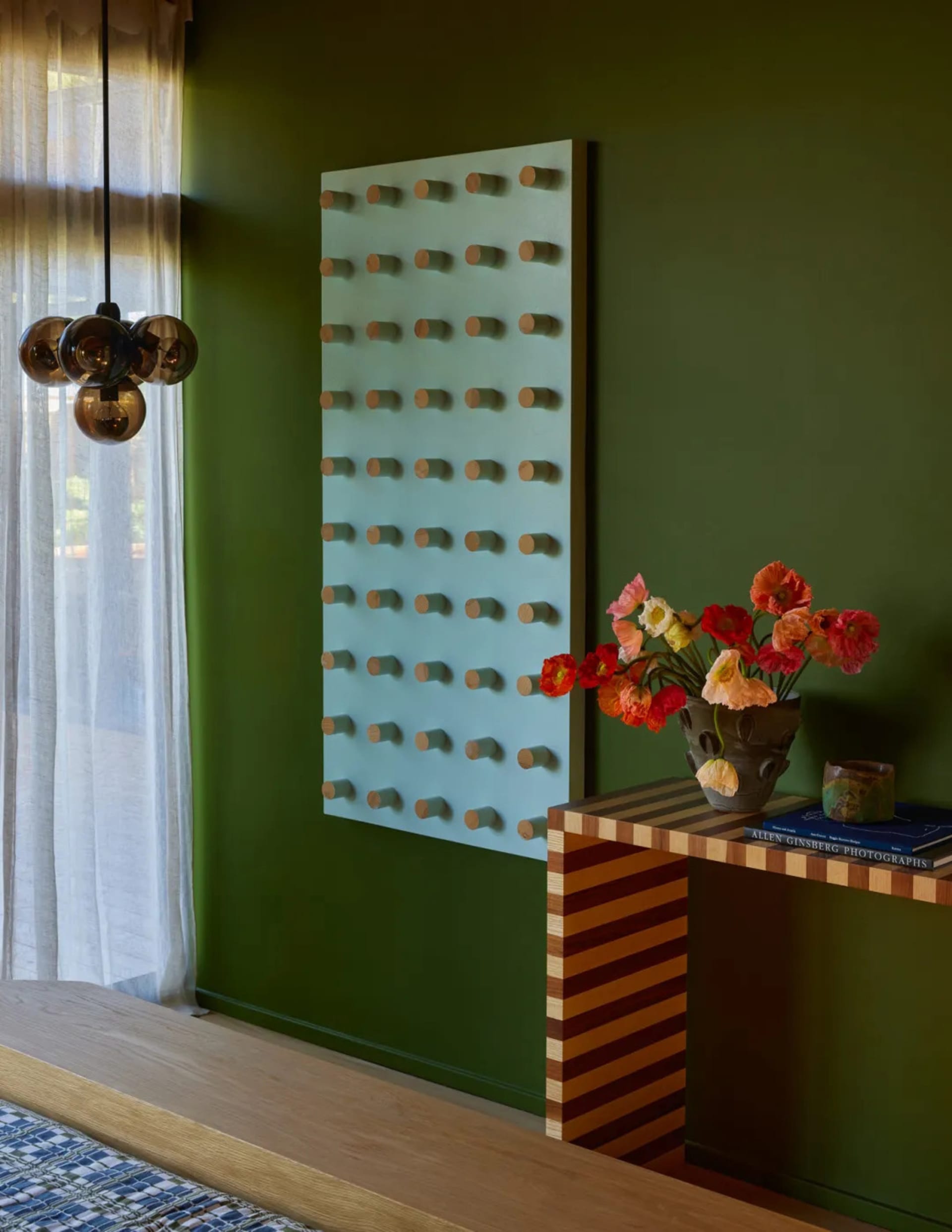 A cozy living space with a green accent wall, a striped table, a large mirror, and flowers in a vase