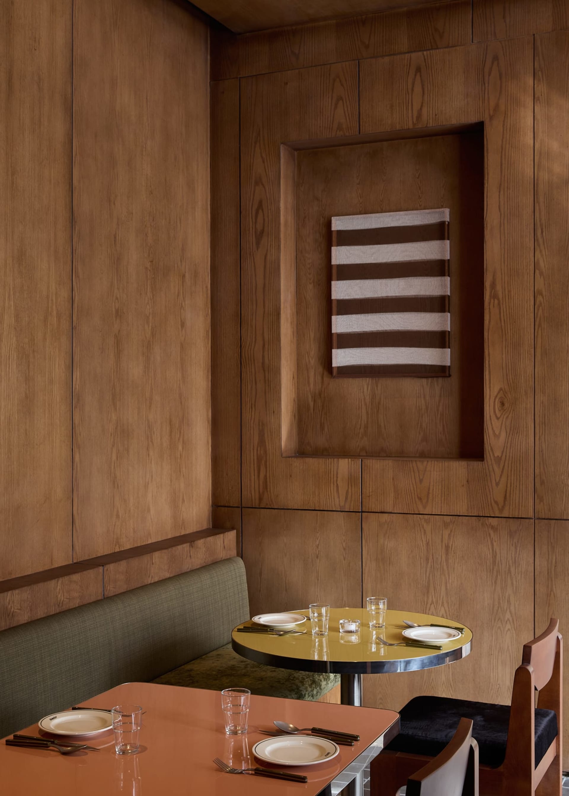 A modern dining room with a wooden table and chairs, set with plates, glasses, and utensils, surrounded by wooden walls and soft, diffused lighting