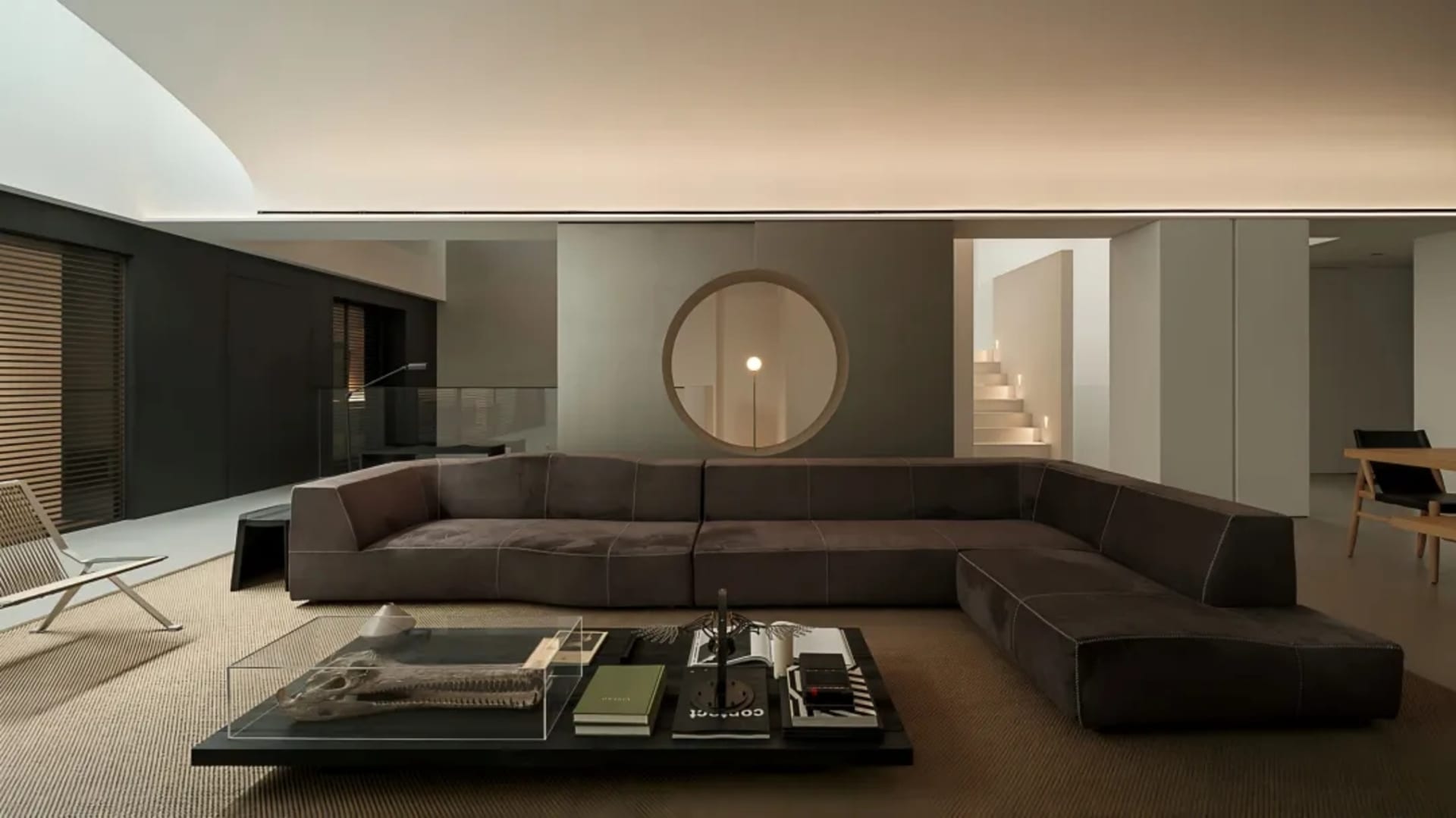 A well-lit modern living room with a leather sofa, a round mirror, a coffee table, and a chair, creating an inviting and comfortable atmosphere