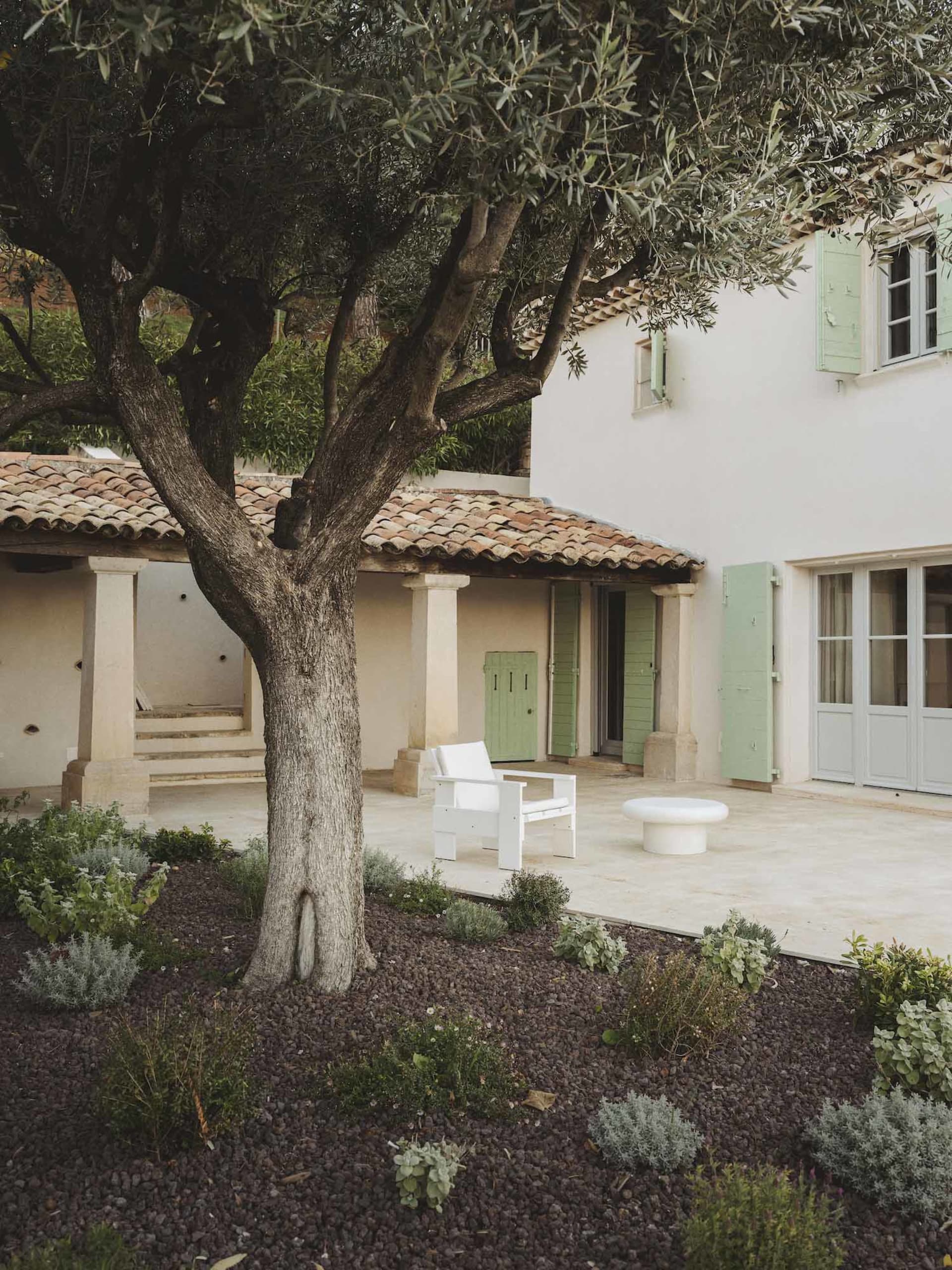 A modern house with a green door and a white chair on the patio, set in a residential area with a garden-like atmosphere