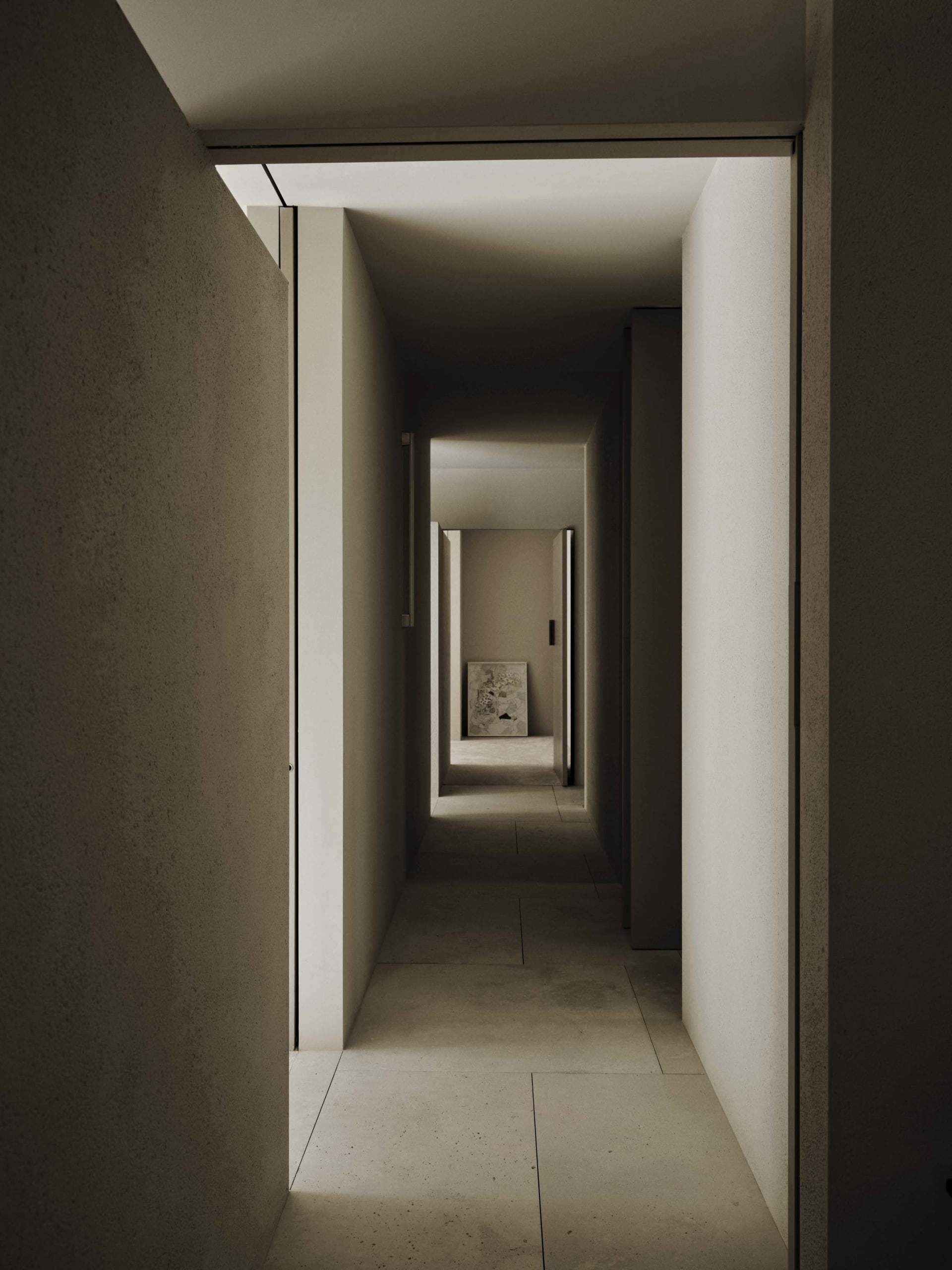 Narrow hallway with a stone floor, a chair, and a cat, in a dimly lit space with a white color scheme