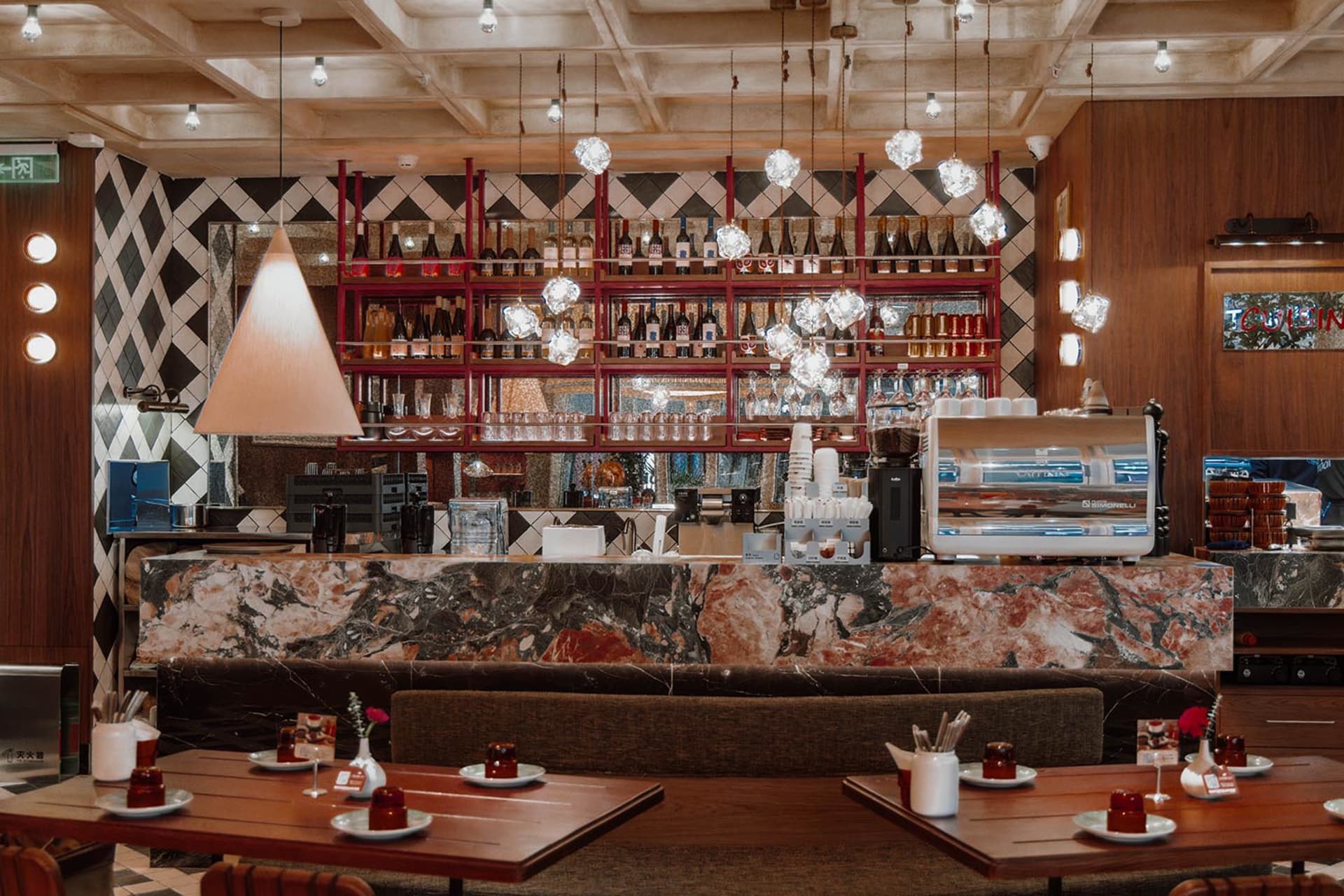 Modern restaurant interior with a marble bar, wooden elements, and dim lighting, featuring tables and chairs for guests