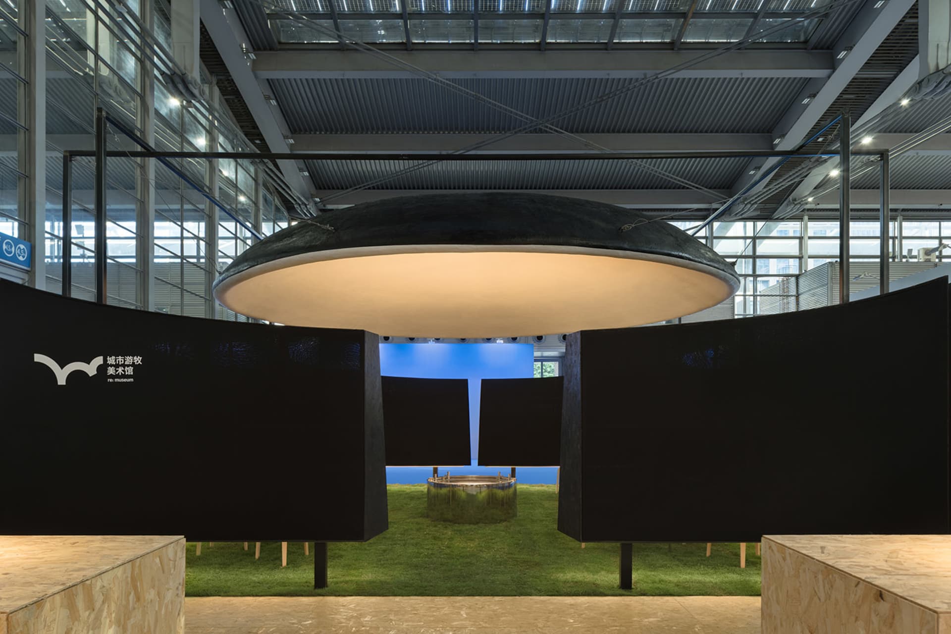Modern art gallery with a blue floor, black ceiling, and a large window, featuring a display of artwork in a well-lit space