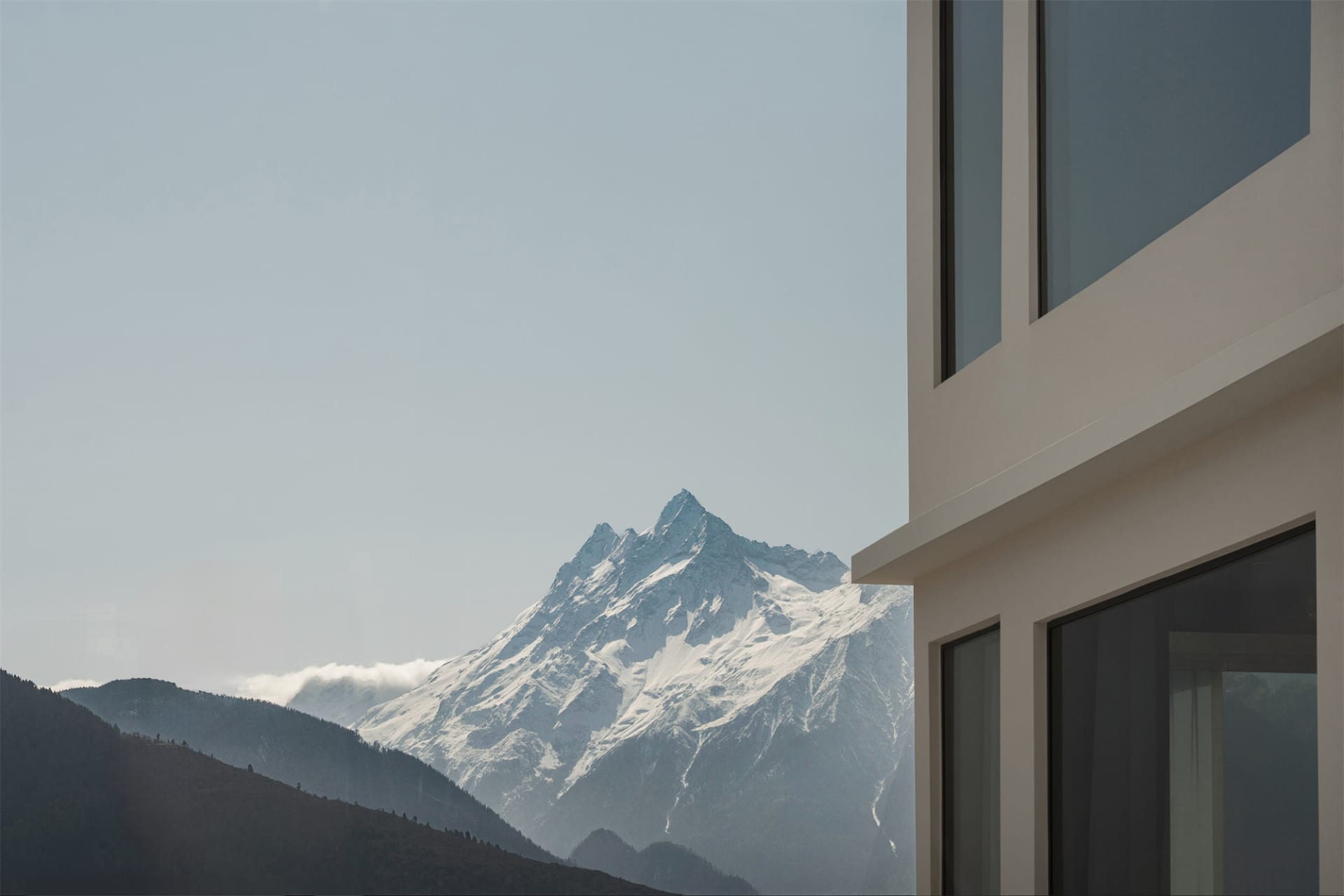 一座現代建築，外牆為混凝土，背景為藍天與覆雪的山峰
