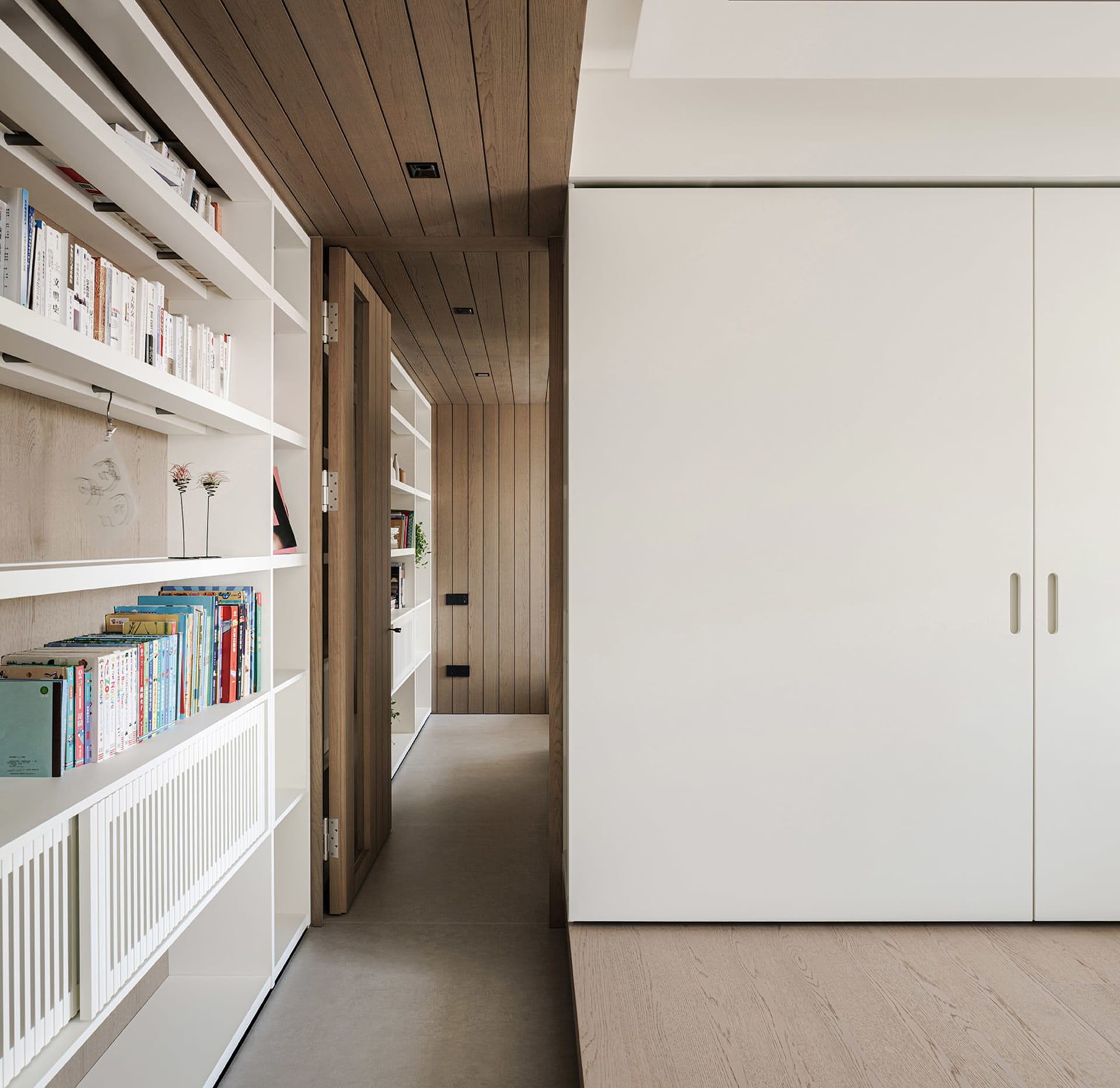 Cozy living space with a wooden floor, a white door, and a bookshelf filled with books in various positions