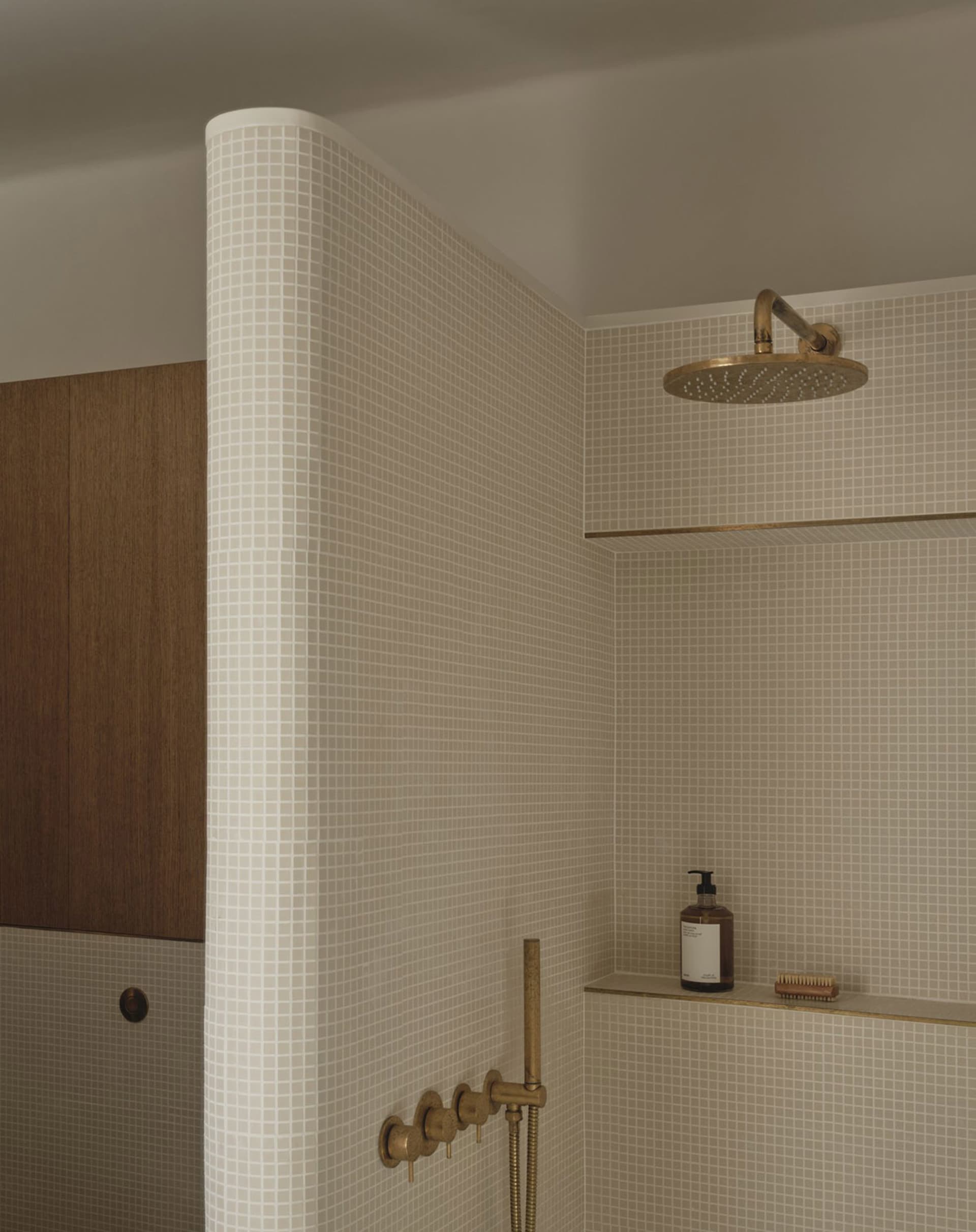 A well-lit bathroom with a white tile wall, a gold shower head, and a bottle on the wall, creating a modern and luxurious atmosphere