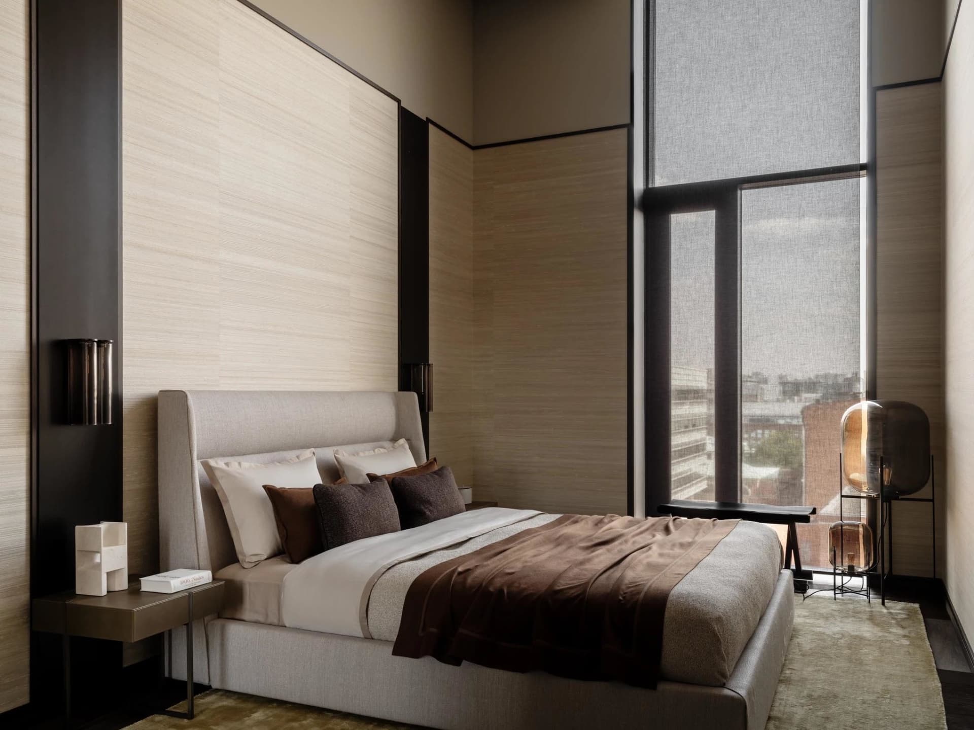 A modern bedroom with a wooden floor, a brown wall, and a bed covered in a brown blanket with pillows, near a window with natural light