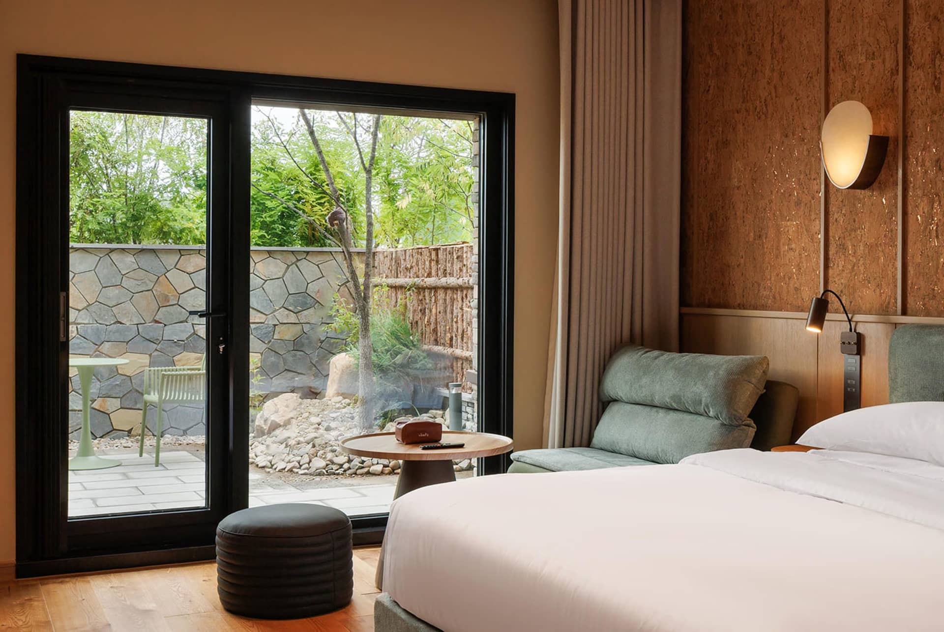 A modern bedroom with a white bed, a wooden chair, and a window allowing natural light to enter, creating a bright and inviting atmosphere