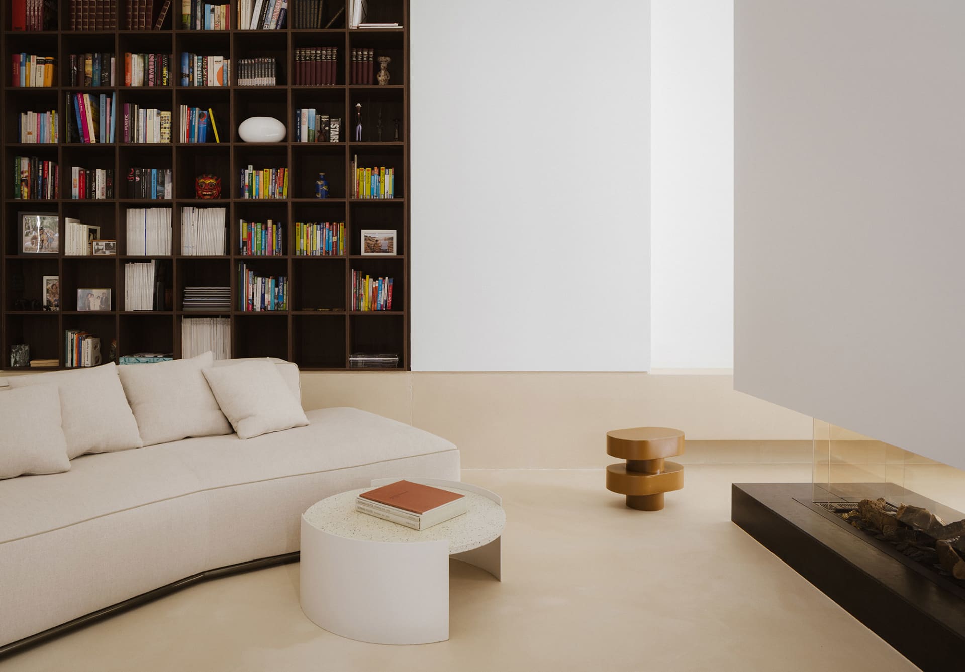 Cozy modern living space with a white color scheme, a couch, a chair, and a bookshelf, lit by natural light from a window