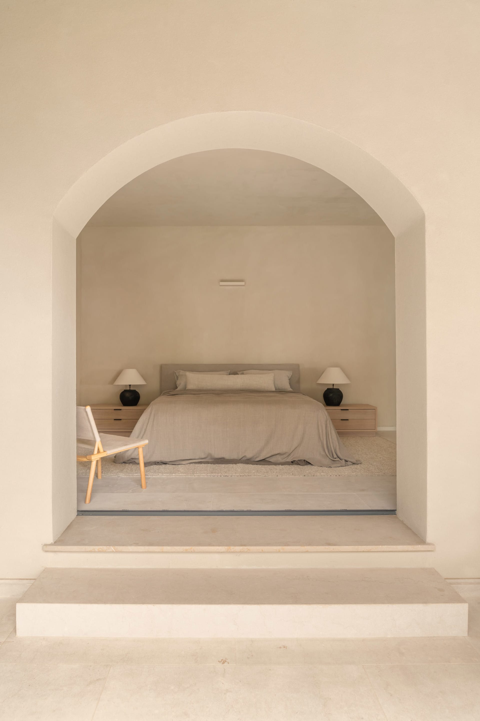 A cozy bedroom with a bed, chair, and lamp, featuring wood and fabric materials, soft lighting, and a focus on relaxation