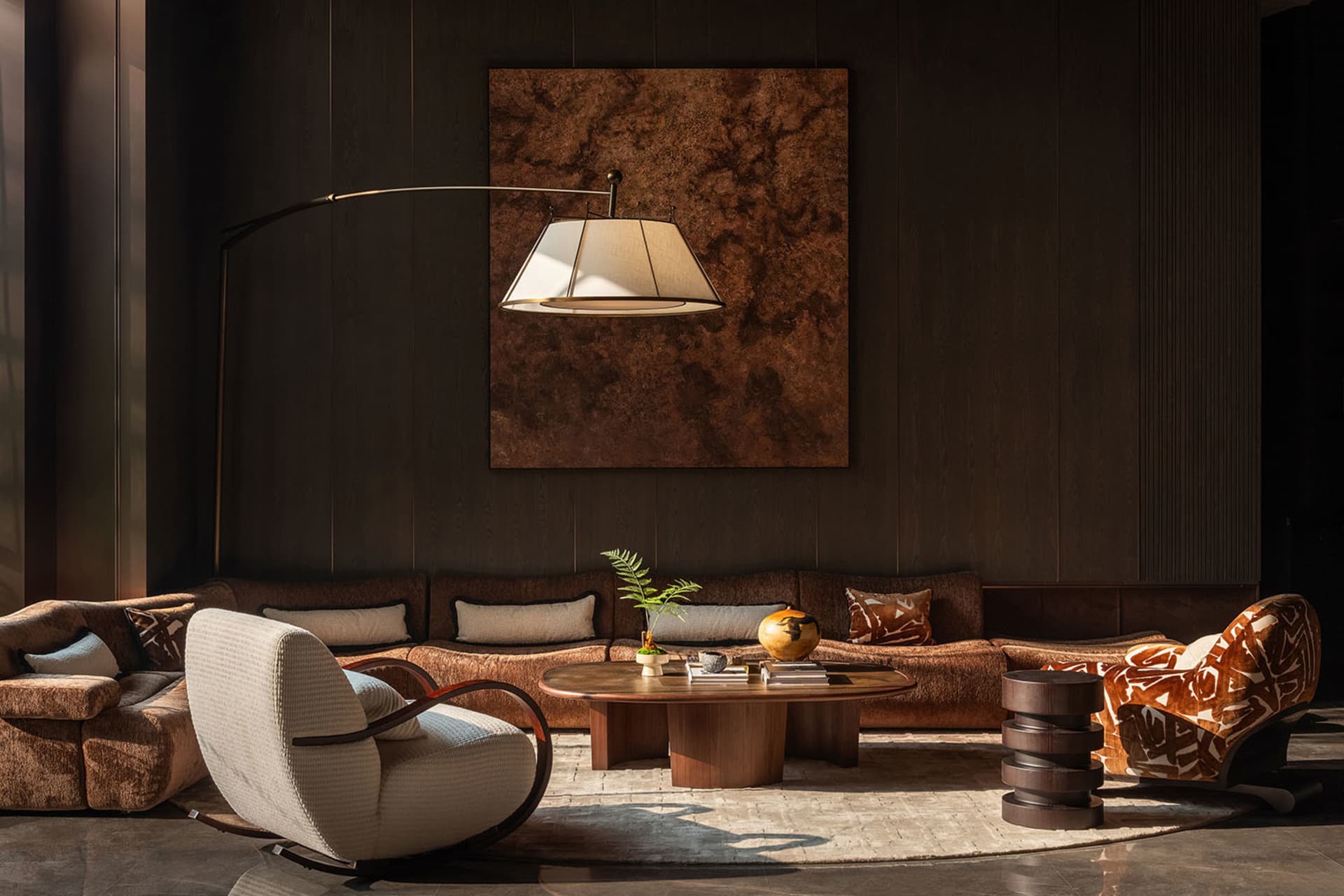 Comfortable living space with a brown couch, chair, and lamp, decorated with a vase, bowl, and book, in a modern and contemporary style with a warm and cozy atmosphere