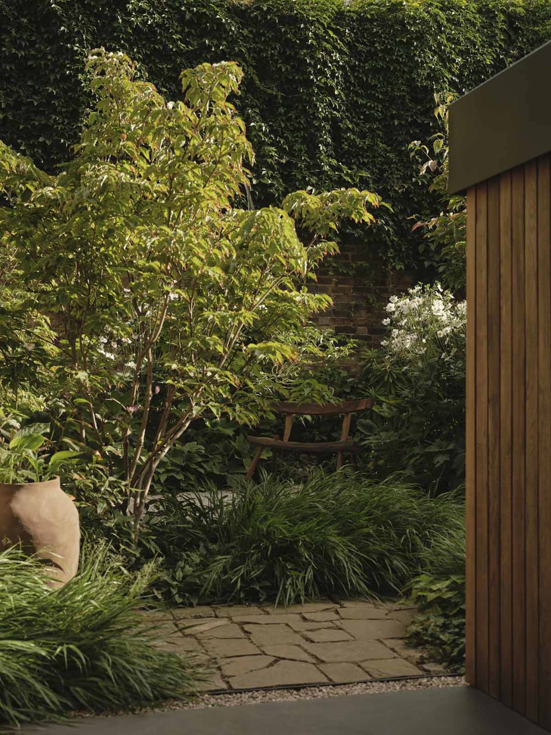 a serene garden setting with a brick patio and a wooden bench surrounded by lush green plants and flowers