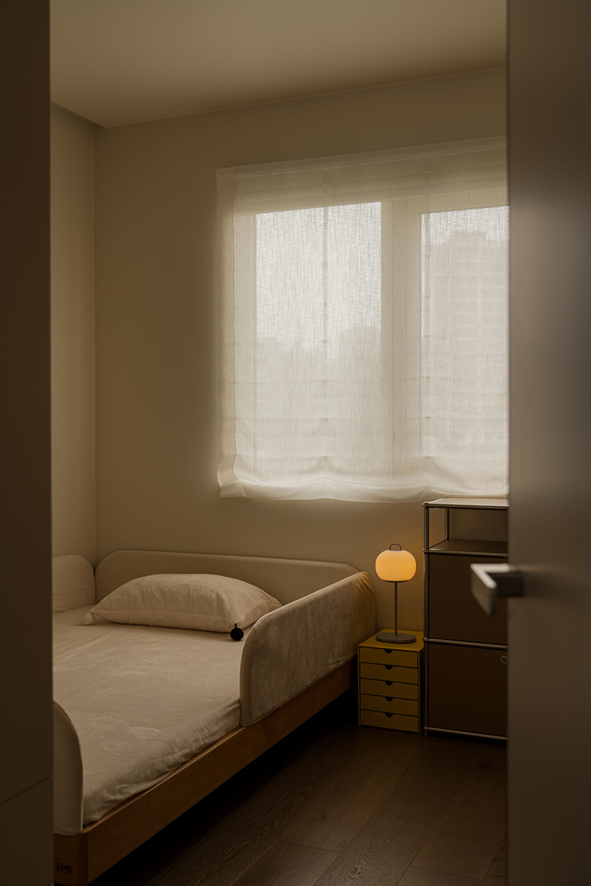 Cozy bedroom with a bed, nightstand, and open window, dimly lit with a yellow lamp on the nightstand