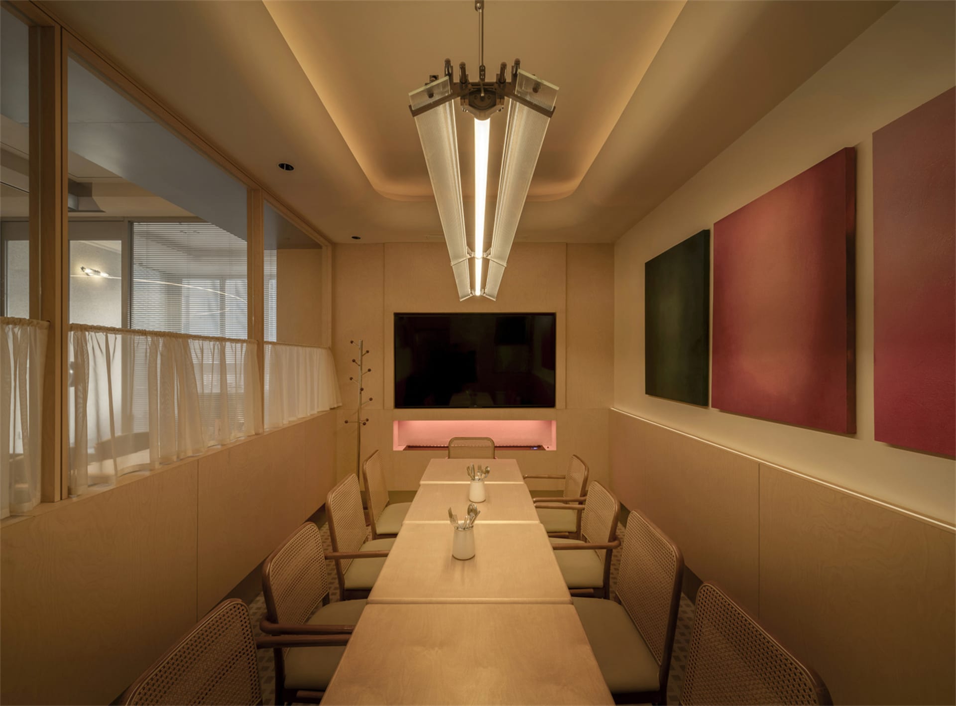 Dimly lit dining room with a wooden dining table and chairs, a television on the wall, and a cozy atmosphere