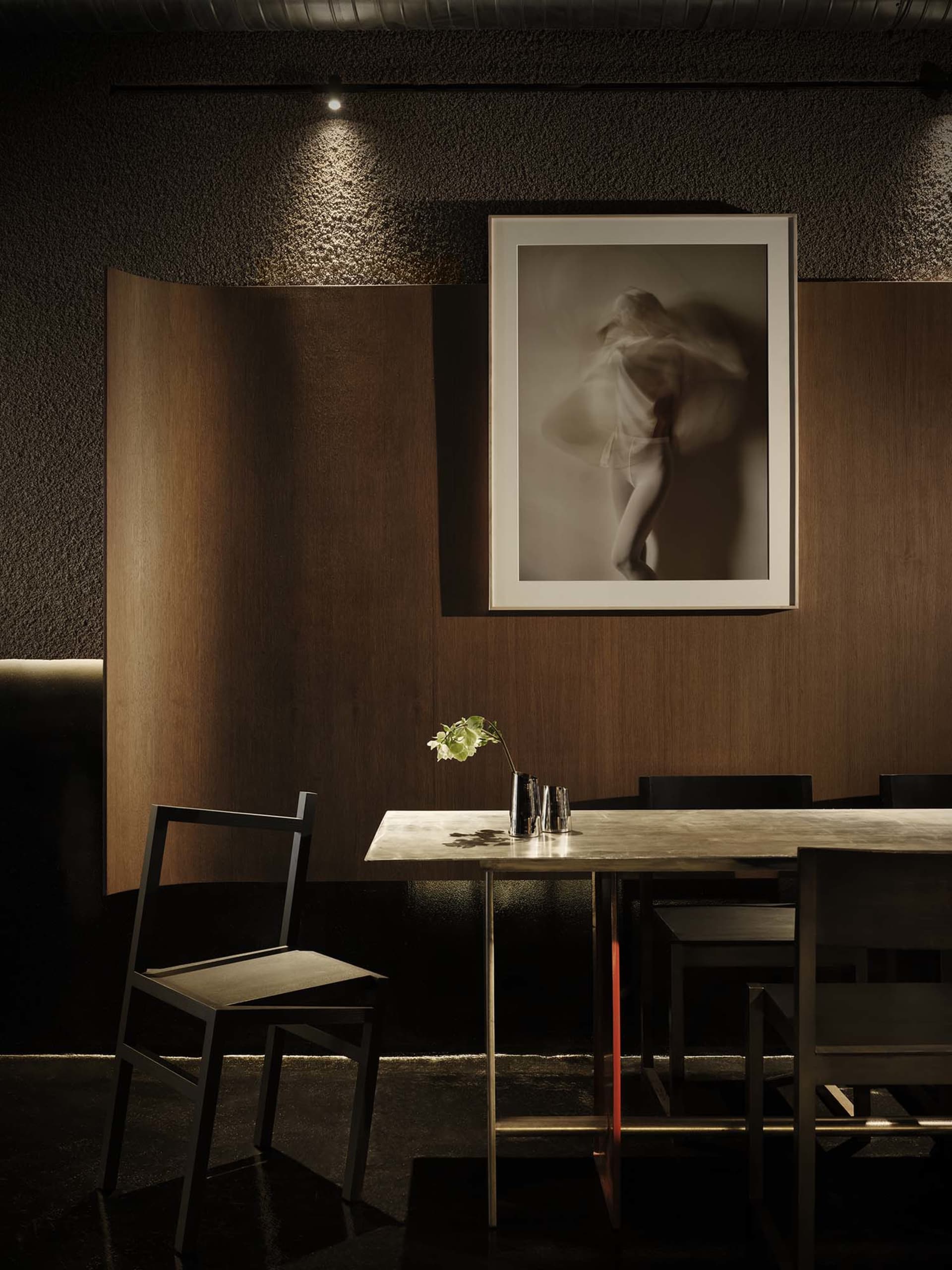 A modern dining room with a wooden floor, a table, chairs, and a picture on the wall, lit by dim lighting