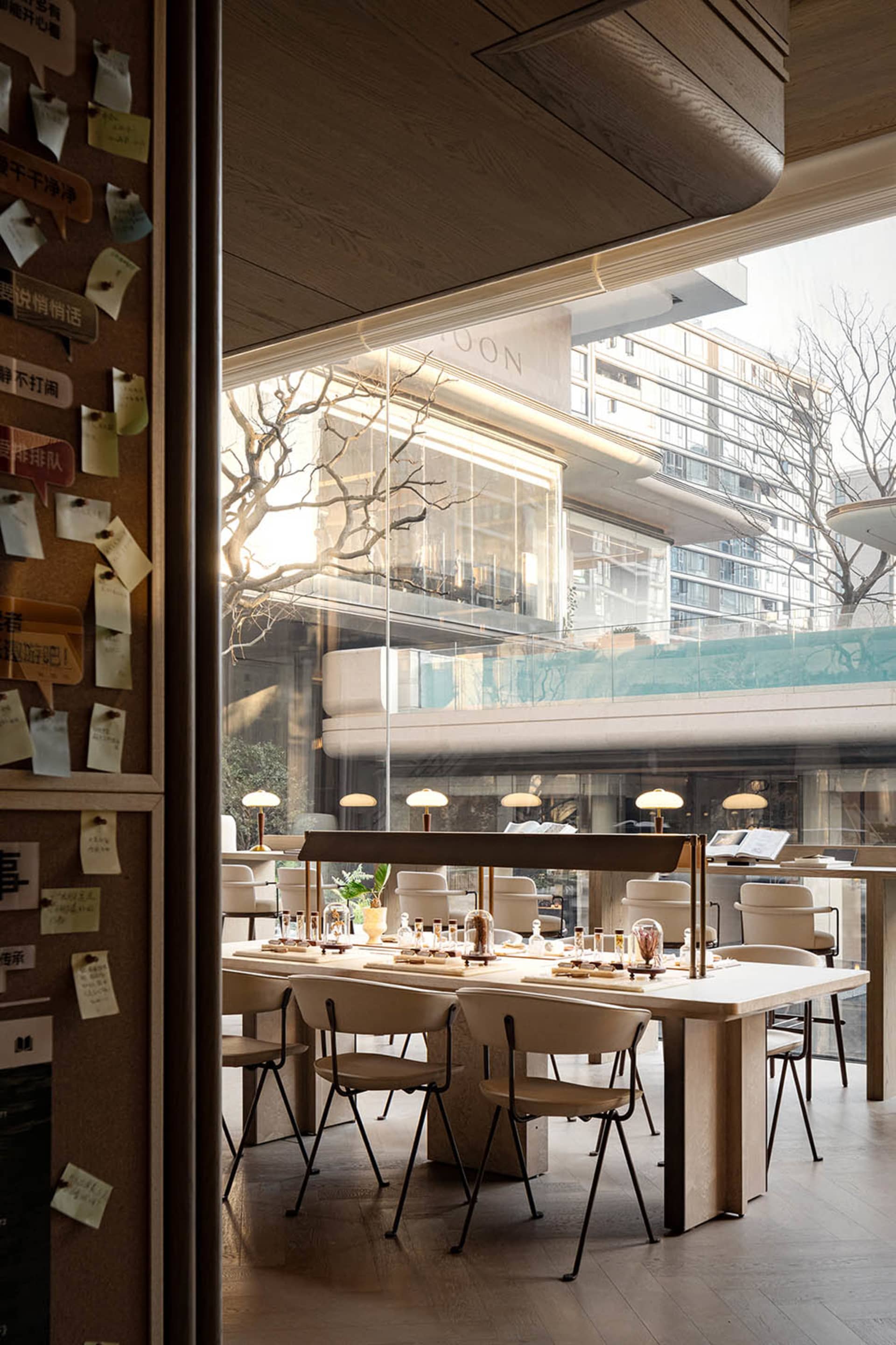 A modern restaurant interior with a large dining table, wooden chairs, and natural light from windows