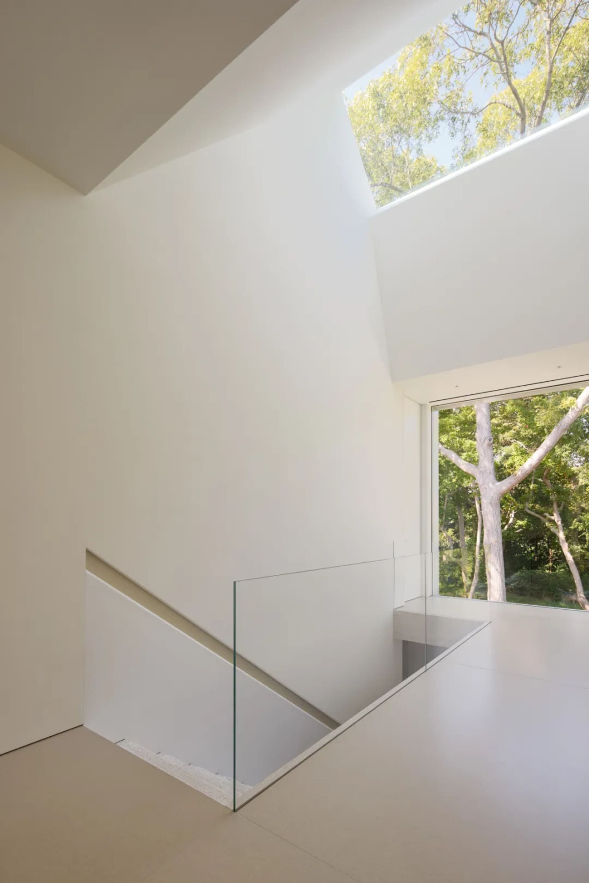 White staircase with a glass railing in a modern minimalist room with a nearby window