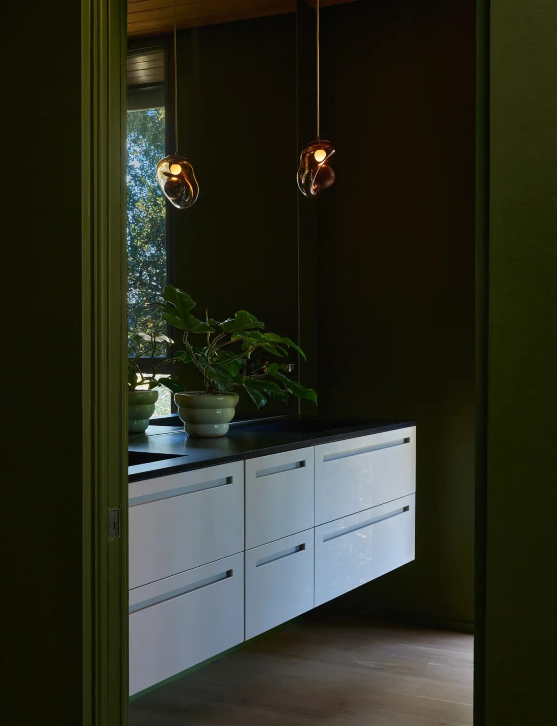 A room with a green wall, black countertop, and green cabinet, featuring a large mirror and a potted plant