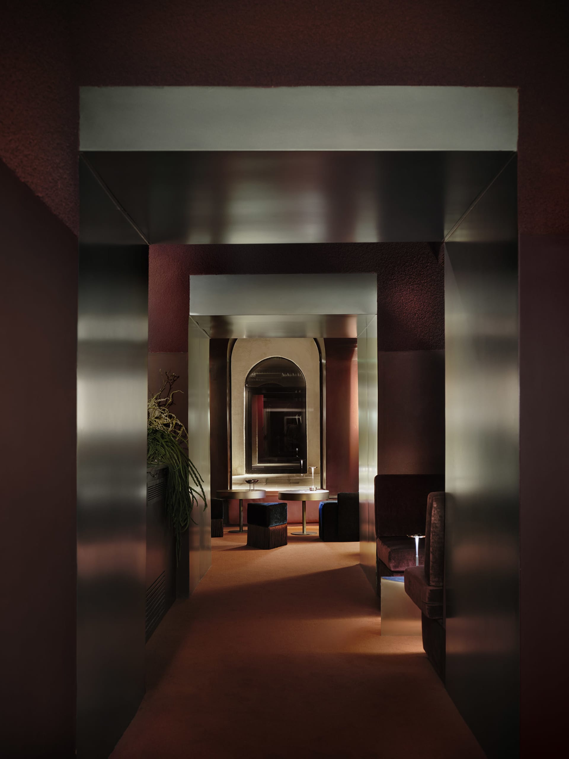 Warm and inviting hallway with red walls, a couch, chair, bench, and a potted plant