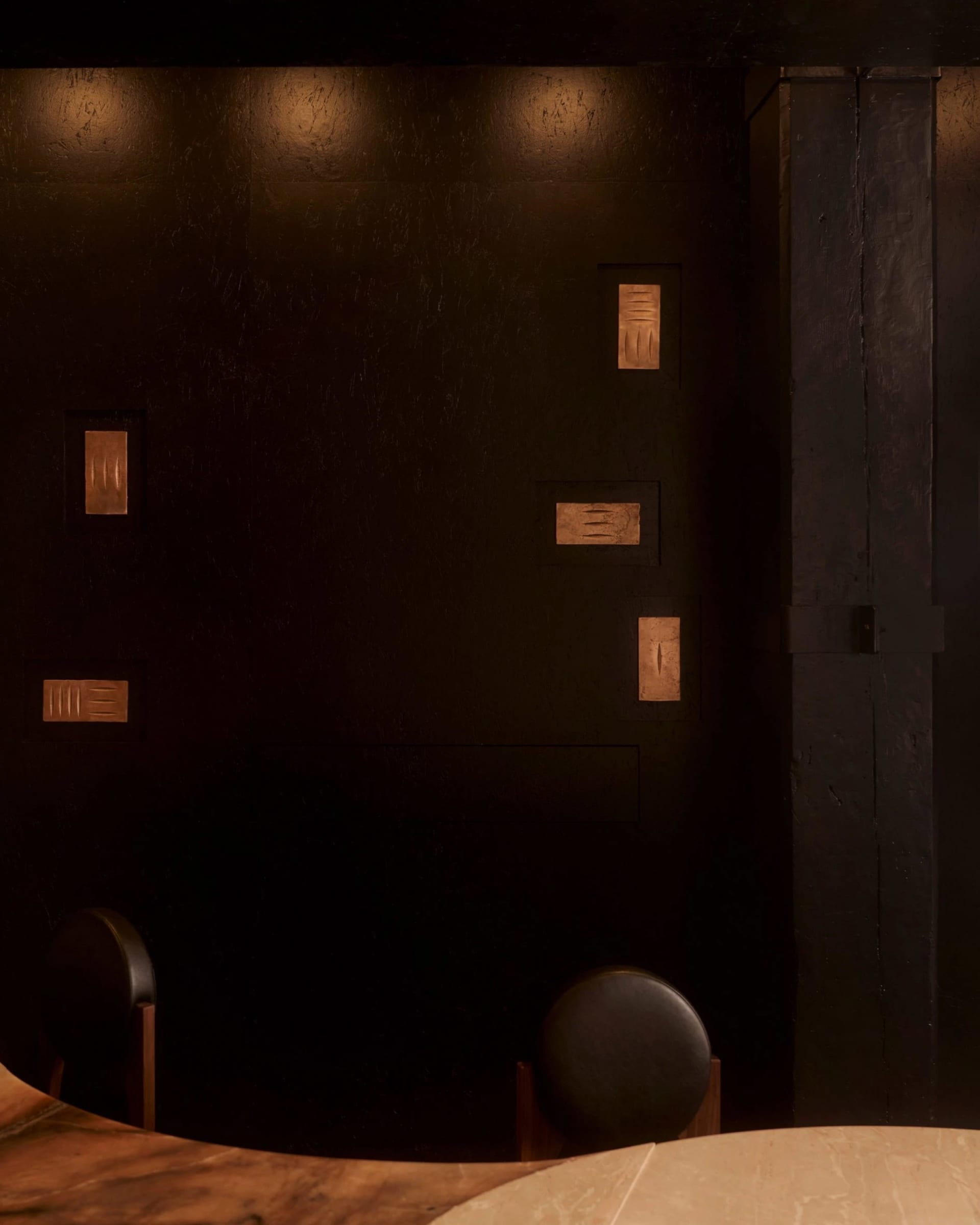 A small, dark room with a black wall and a black chair in the center, creating a minimalist atmosphere