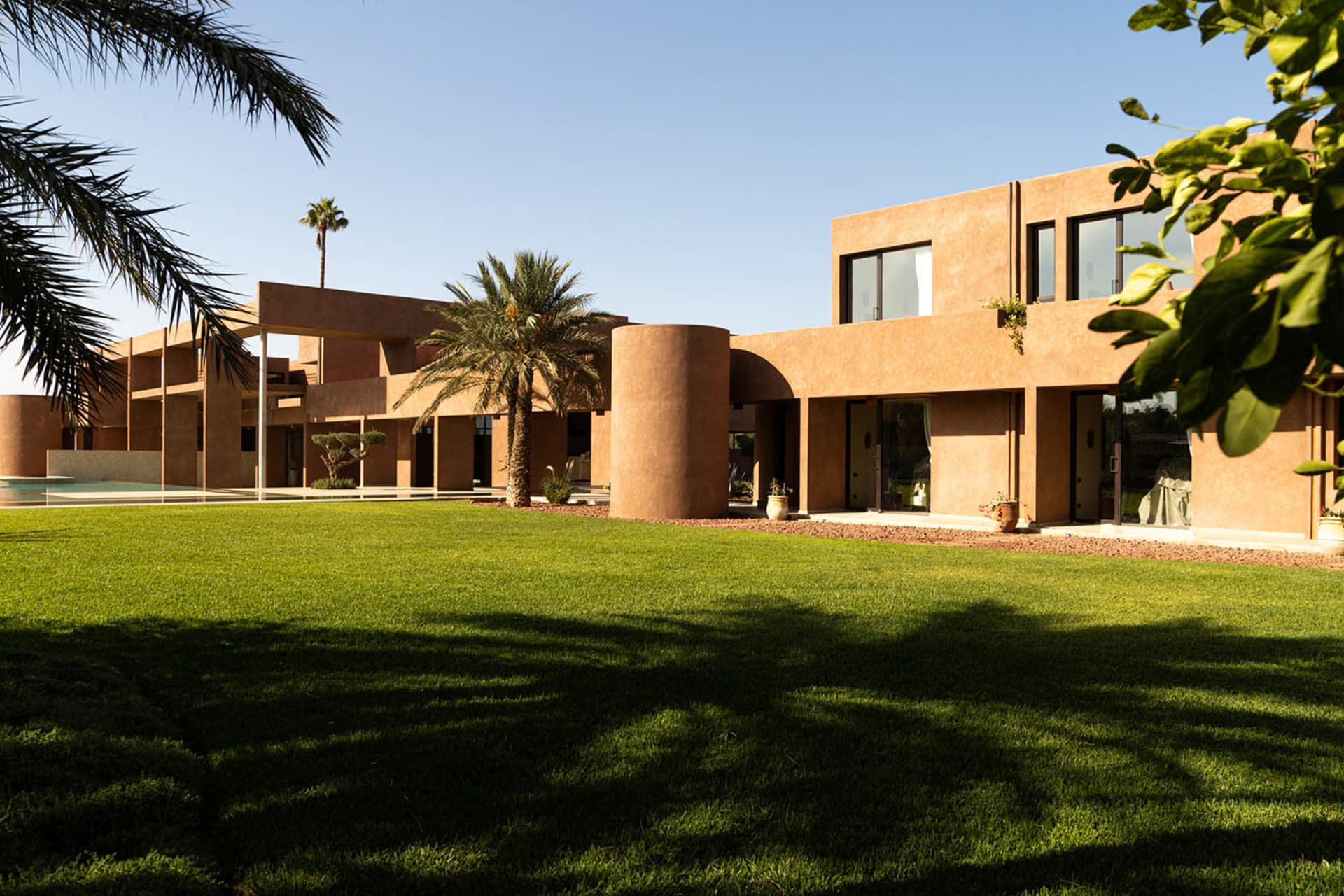A modern house with a brown exterior, surrounded by palm trees and a lush green lawn, with natural light and a clean design