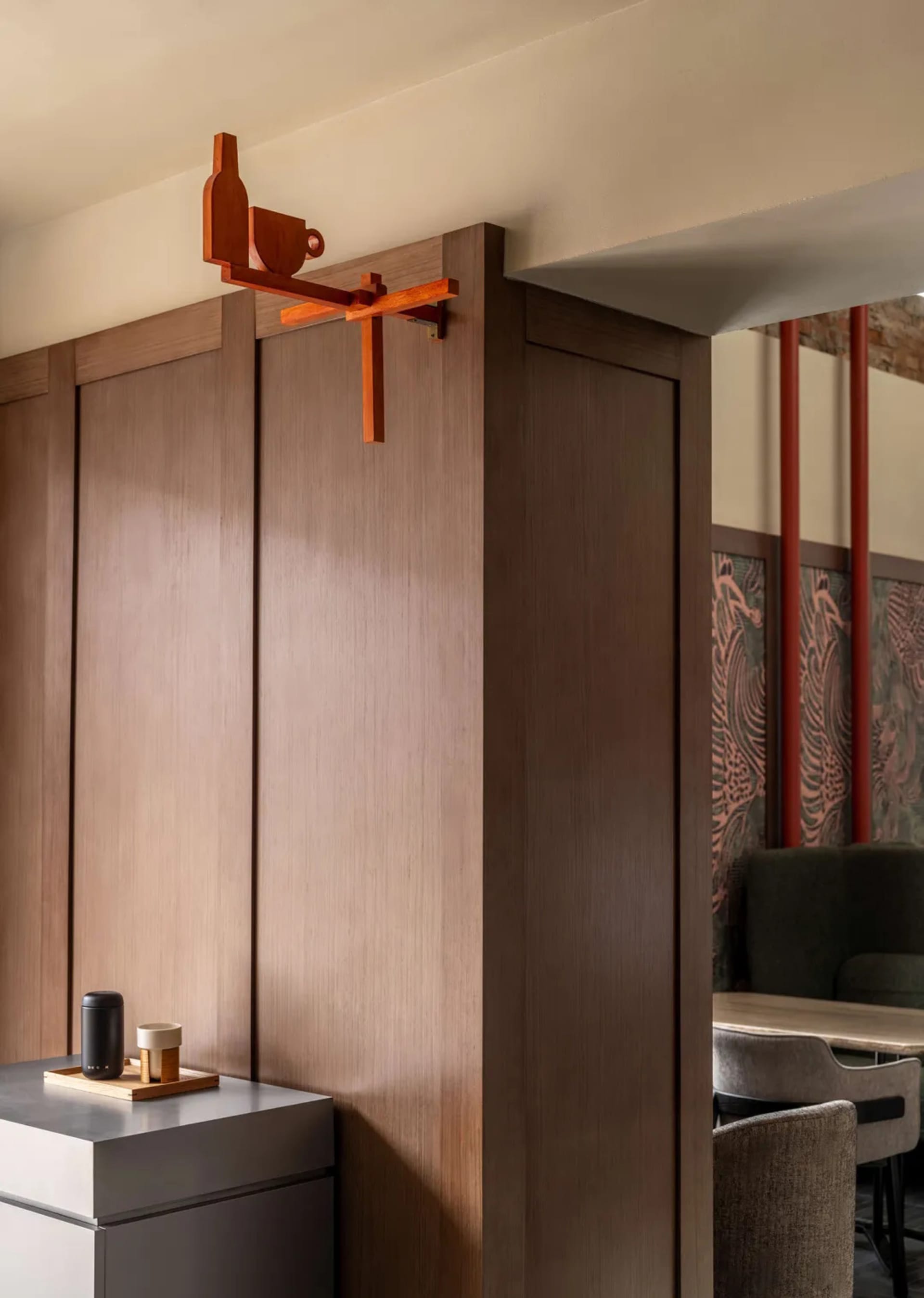 Dining room with a wooden wall, a brown wooden door, a dining table, chairs, a cup, a bowl, and a vase, creating a warm and cozy atmosphere