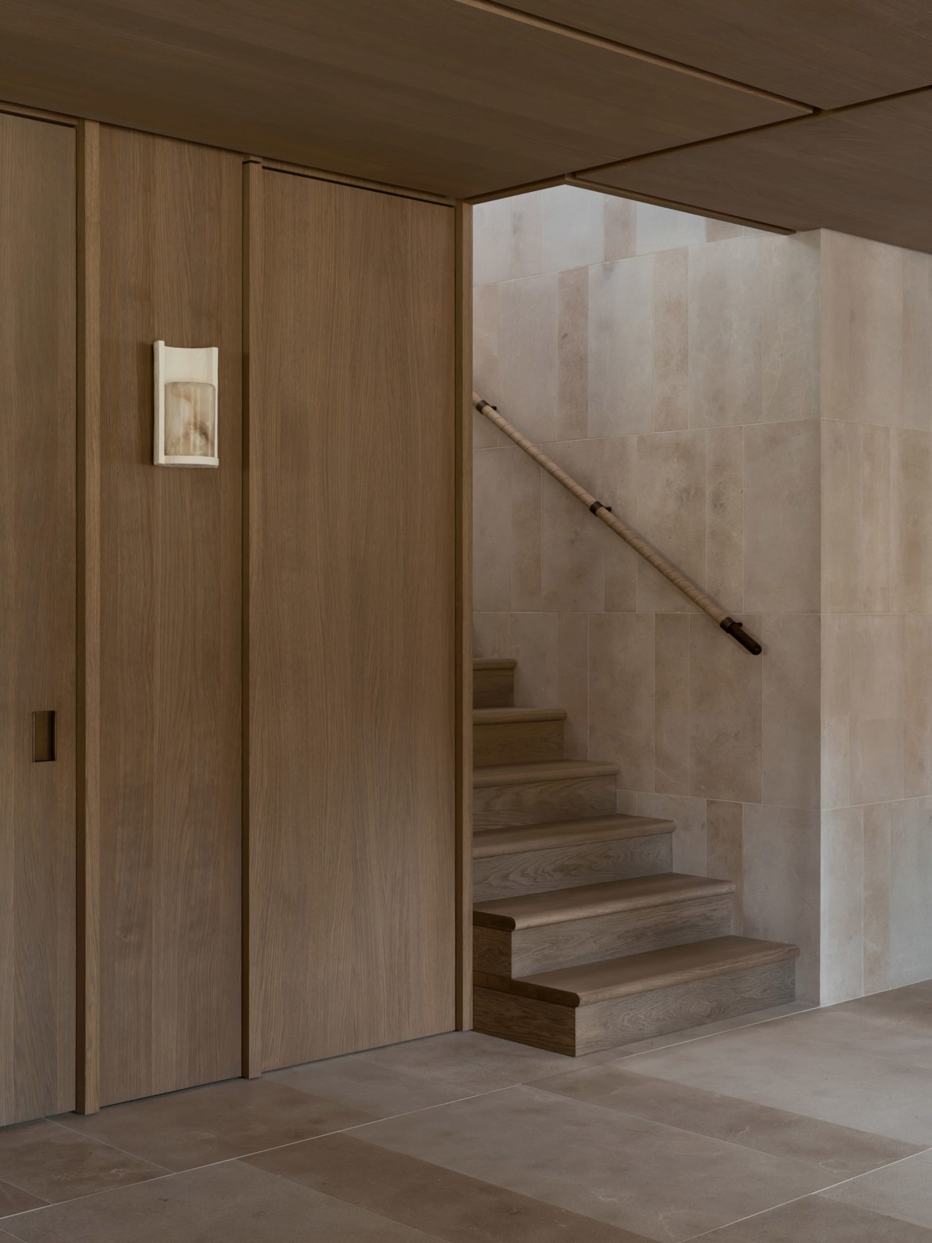 A dimly lit hallway with a wooden staircase and door, surrounded by a wall on one side and a door on the other