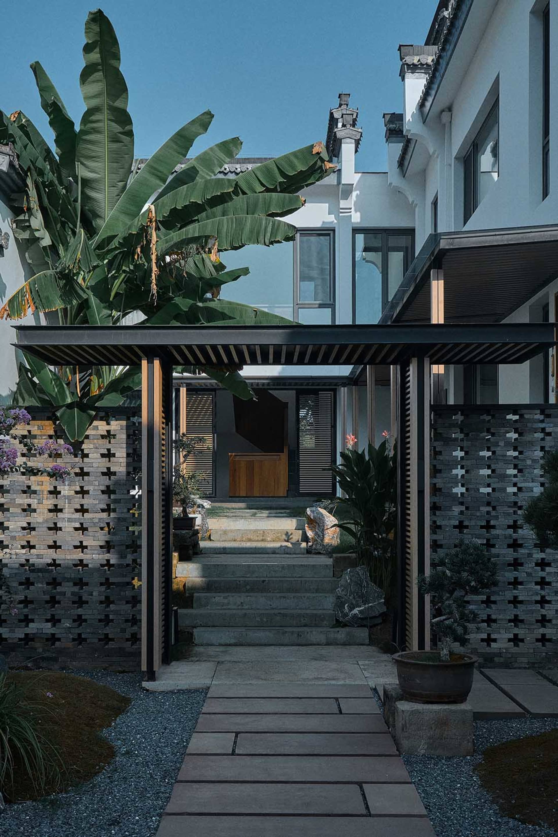A modern house with a black and white color scheme features a patio surrounded by a black fence and potted plants adding a touch of greenery to the space