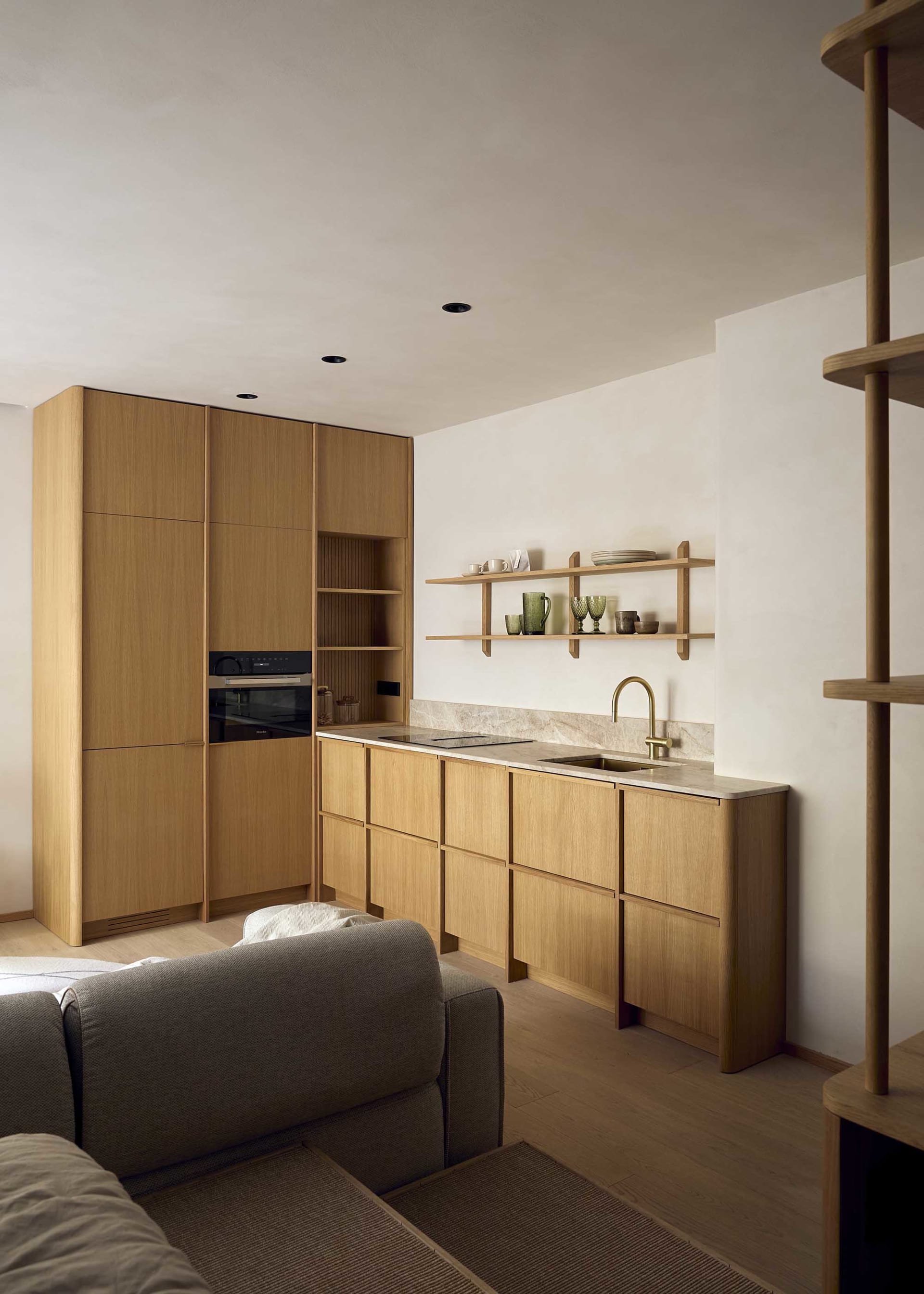 A well-lit kitchen and living room area with wooden cabinets, a couch, and a chair, creating a warm and inviting atmosphere