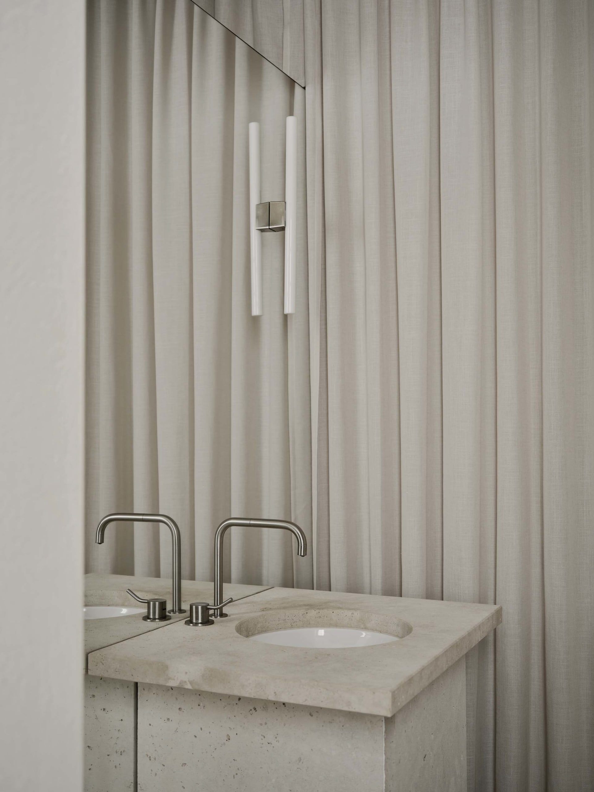 Bathroom with a marble sink under a white curtain, a mirror above, and a white color scheme, lit by natural light