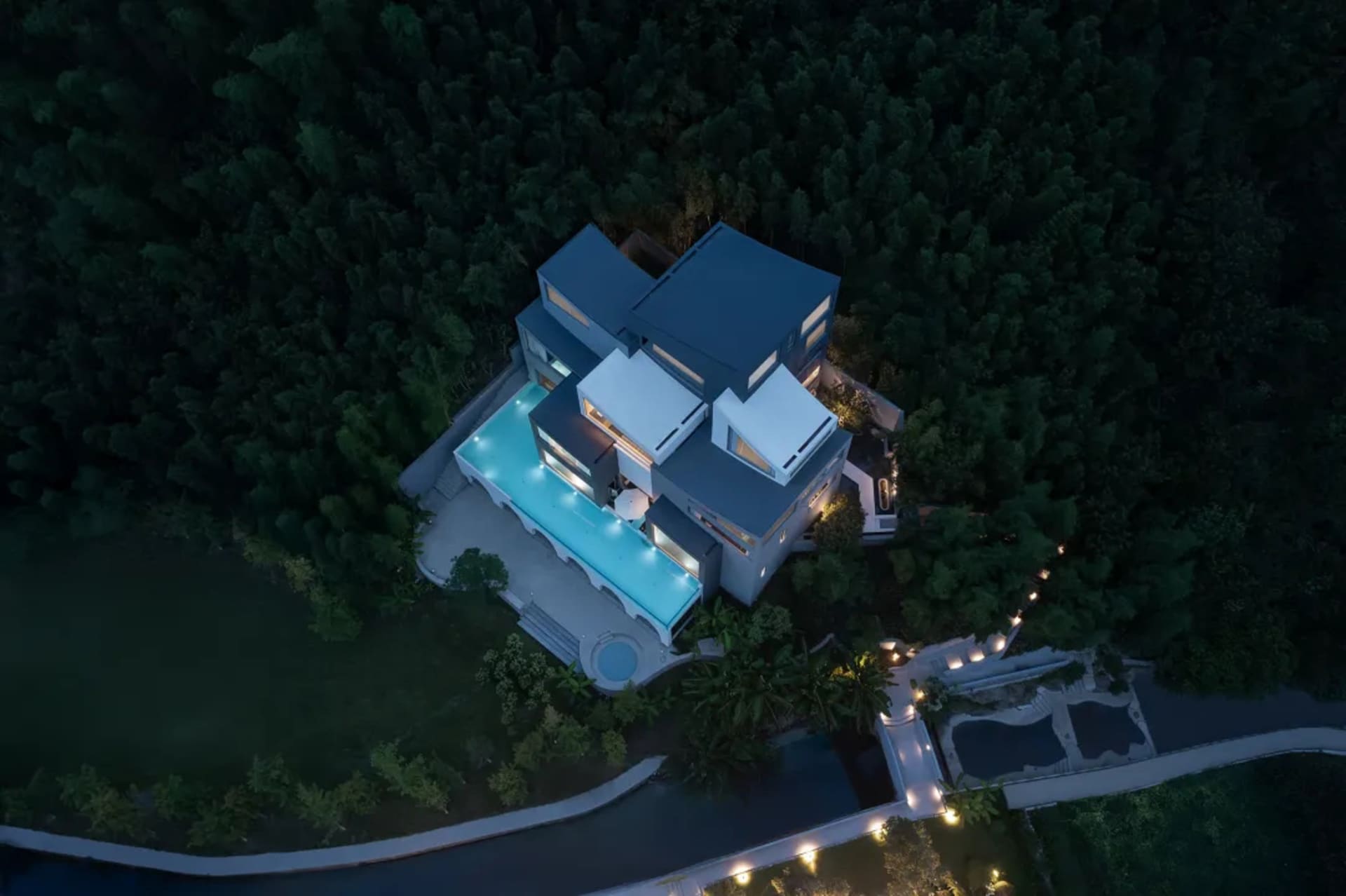 A serene and inviting modern house with a concrete exterior, a blue swimming pool, and a tree-lined backyard