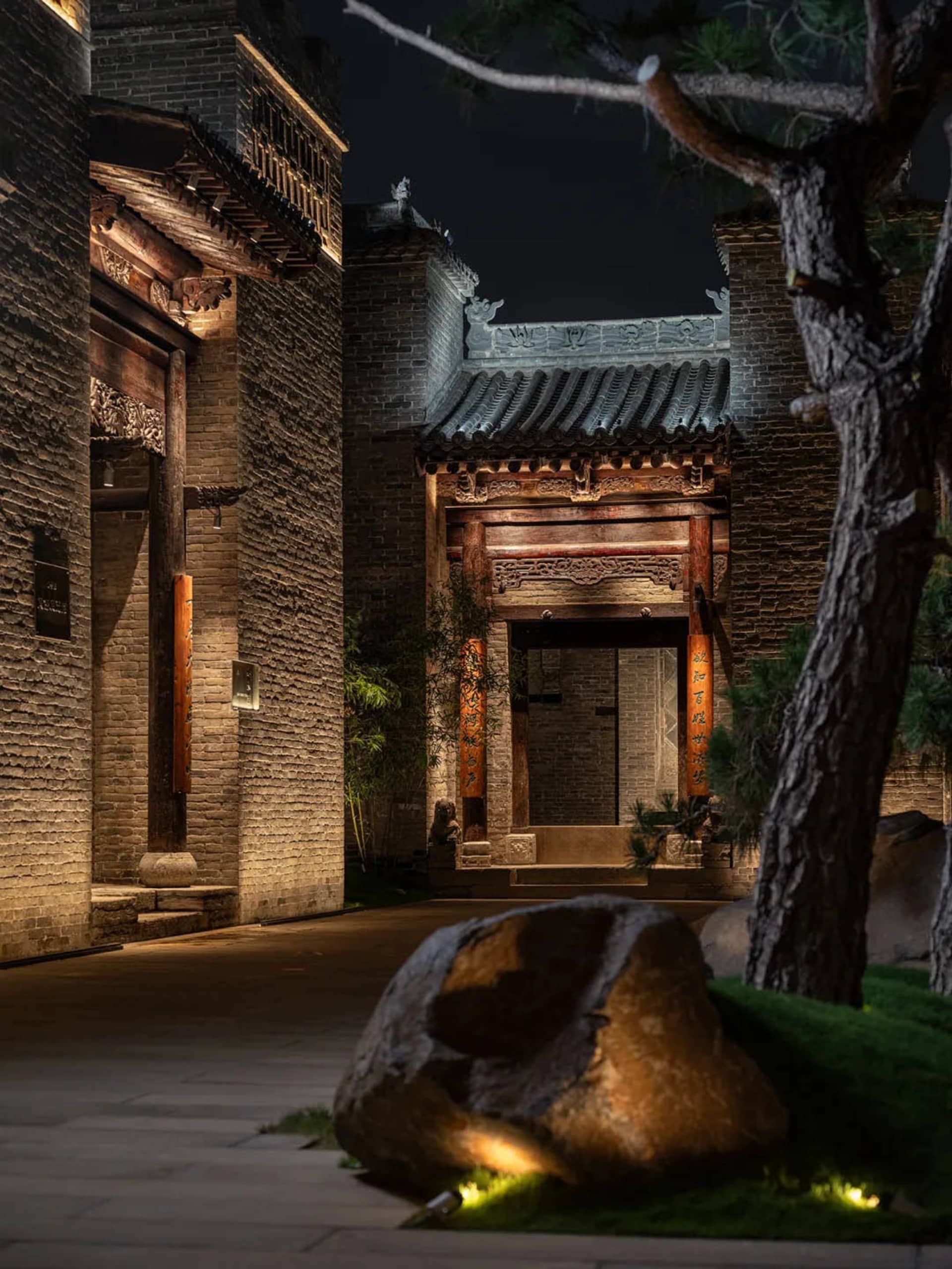 一座傳統中國建築的石材外牆，擁有大型拱門和石板路，低調的光源下
