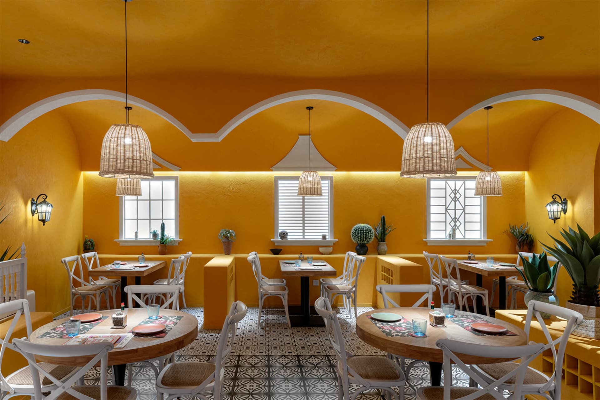A modern restaurant with a warm yellow color scheme, featuring a dining area with tables and chairs, potted plants, and a welcoming atmosphere