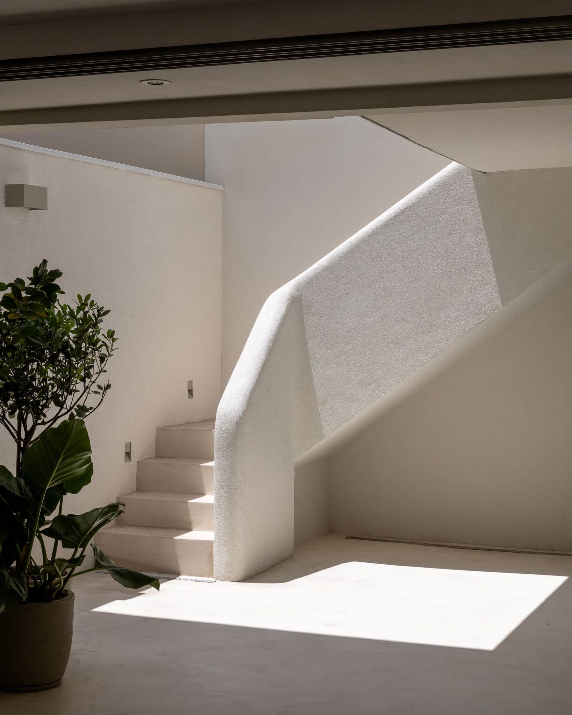 A white staircase in a sunlit area with a concrete staircase and white railing