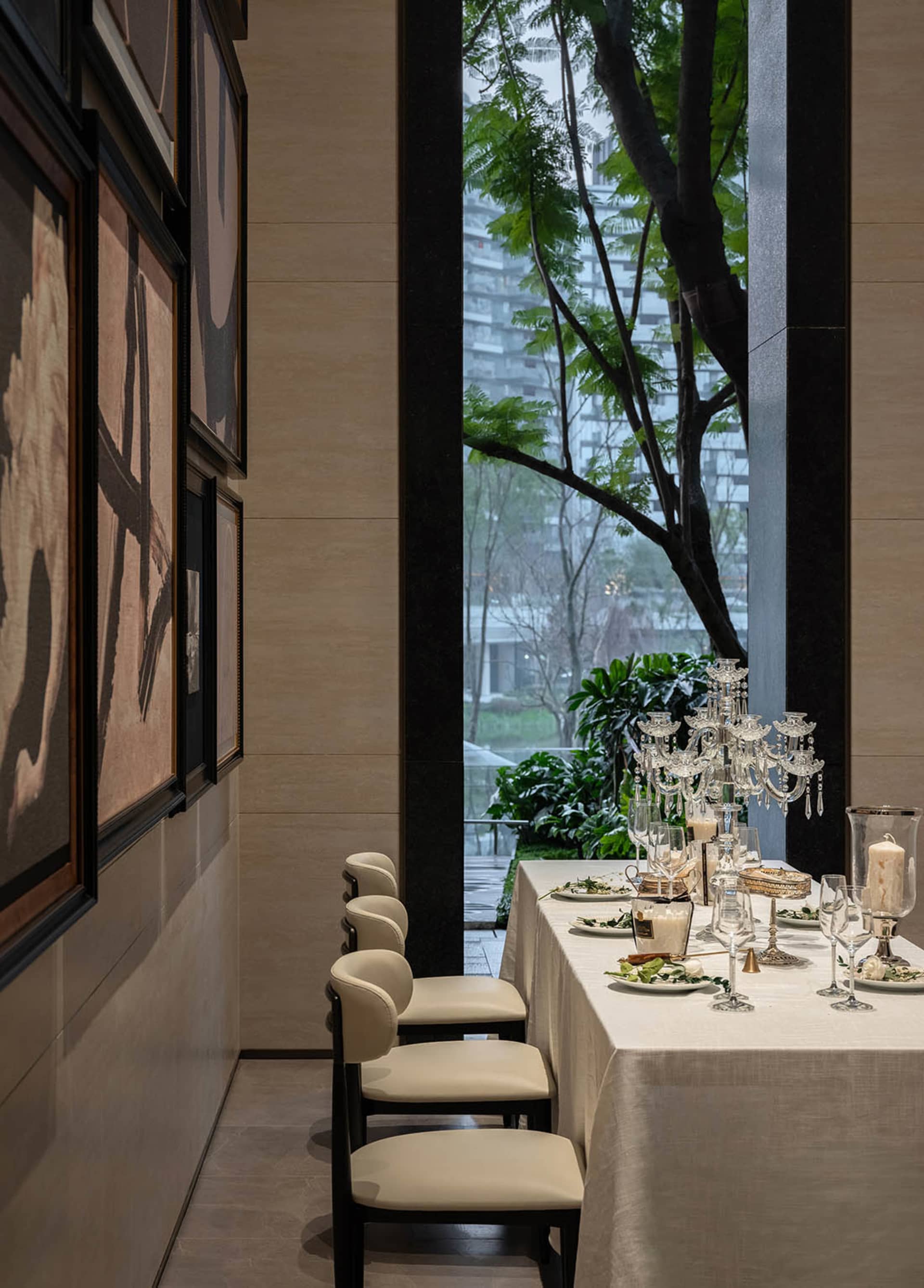 Dining room with a large table set for a meal, surrounded by potted plants and a large window allowing natural light