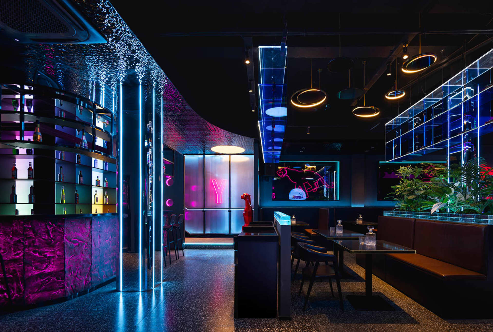 A modern restaurant interior with a bar, large window, and comfortable seating area with wooden furniture and potted plants, creating a warm and inviting atmosphere