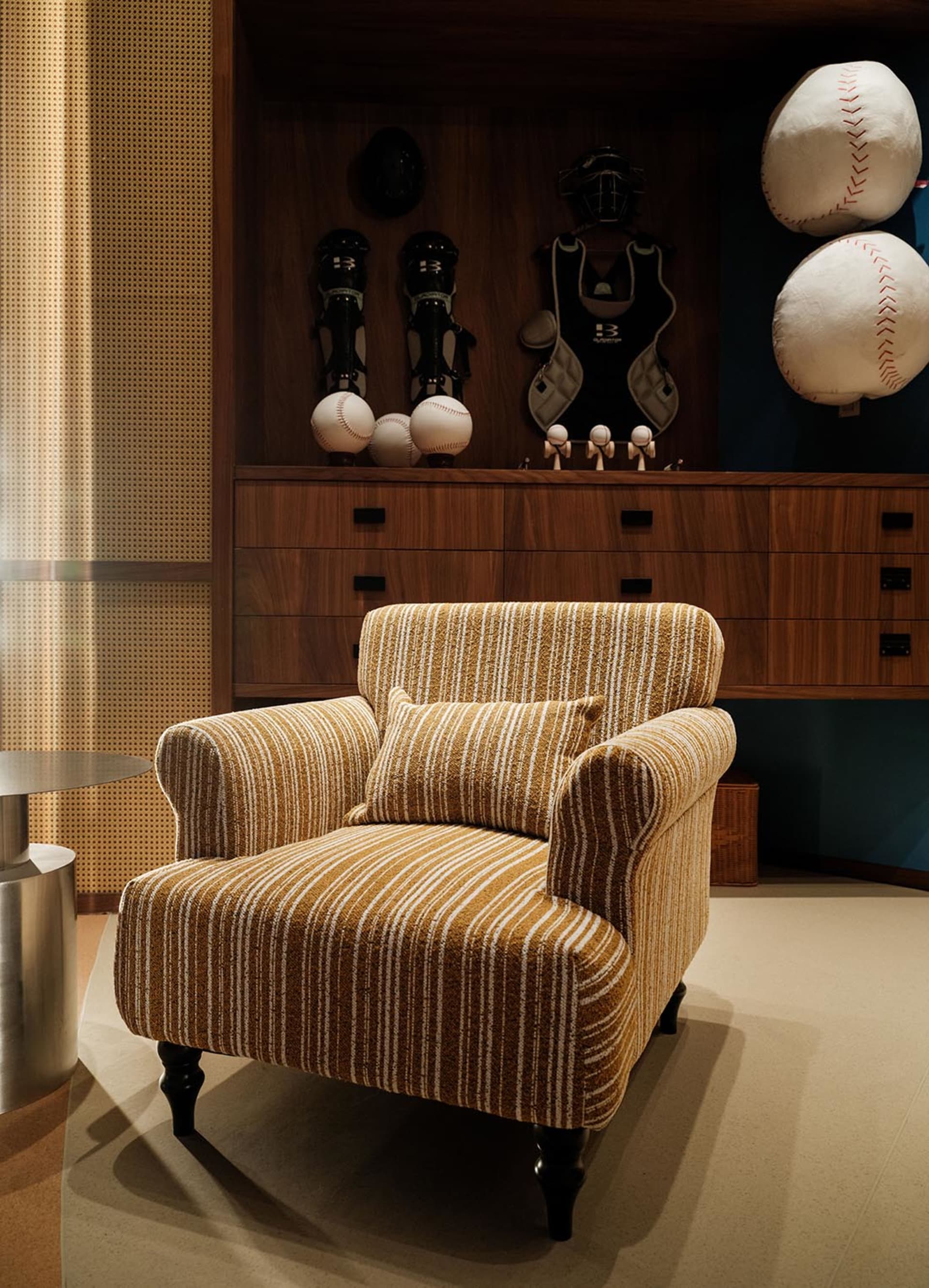 A well-lit living room with a yellow and white striped chair, a table, and a baseball glove on display, creating a cozy atmosphere with a mix of yellow and white colors